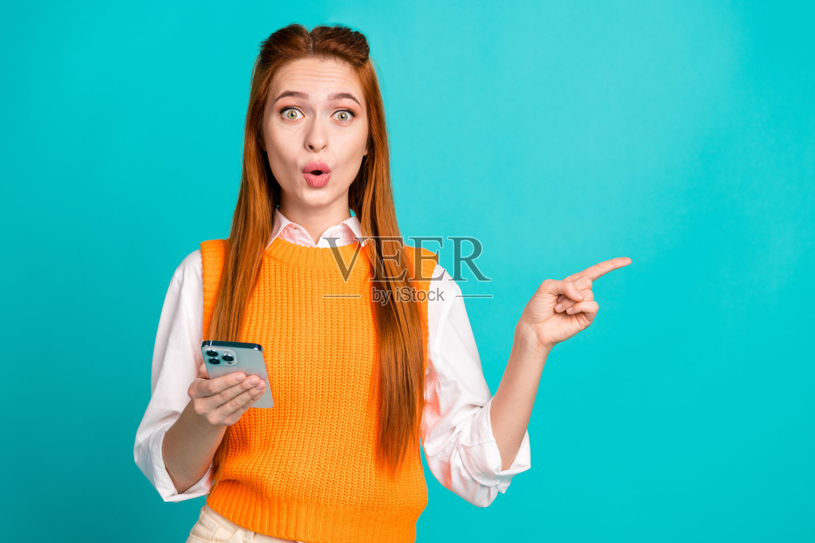 可爱可爱的漂亮女孩穿着时髦的橙色衣服，在青色背景上宣传现代小工具的空白空间照片摄影图片