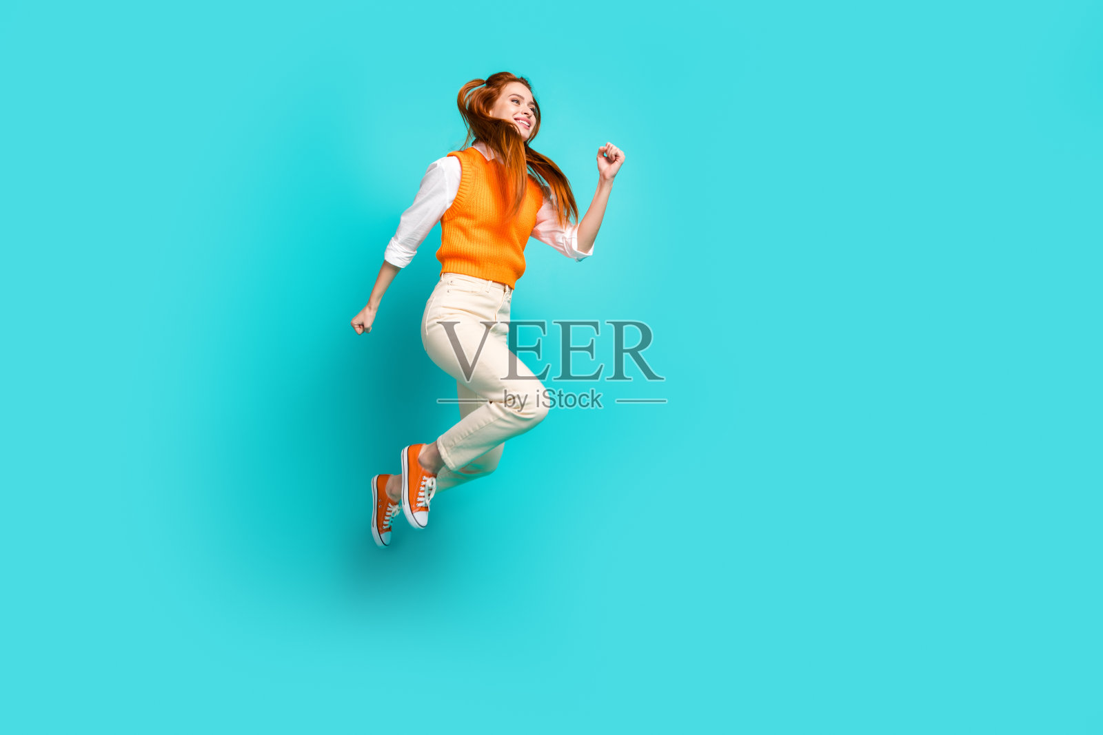 照片中可爱可爱的女孩穿着橙色时髦的衣服跳起来，看起来空白的空间孤立在海蓝宝石色的背景上照片摄影图片