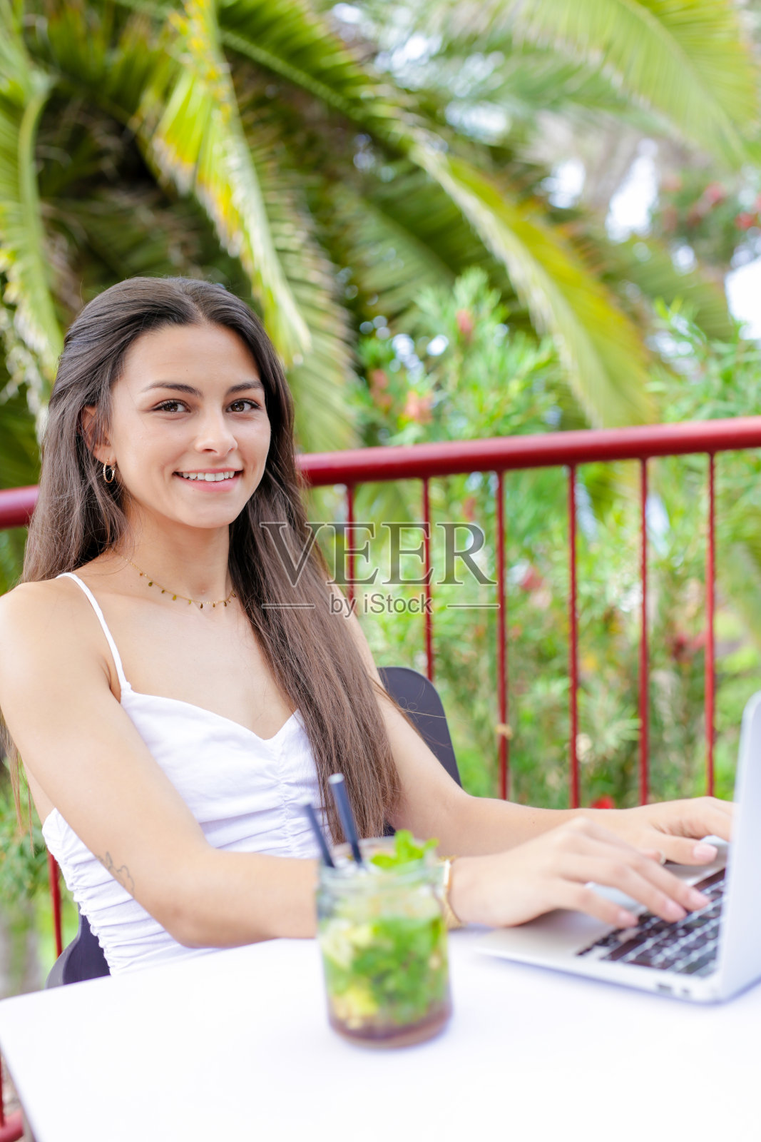 年轻的西班牙女子坐在桌边，手里拿着笔记本电脑和饮料照片摄影图片