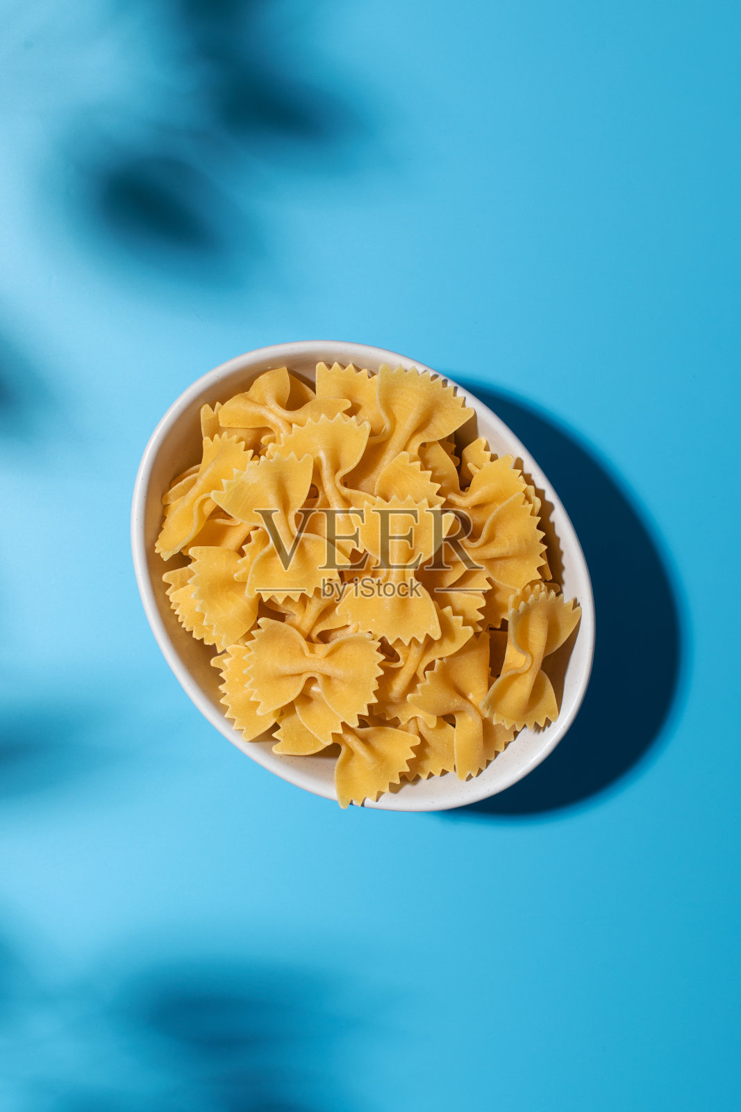 未煮熟的领结意面，落在白色的碗里，蓝色的背景有阴影照片摄影图片