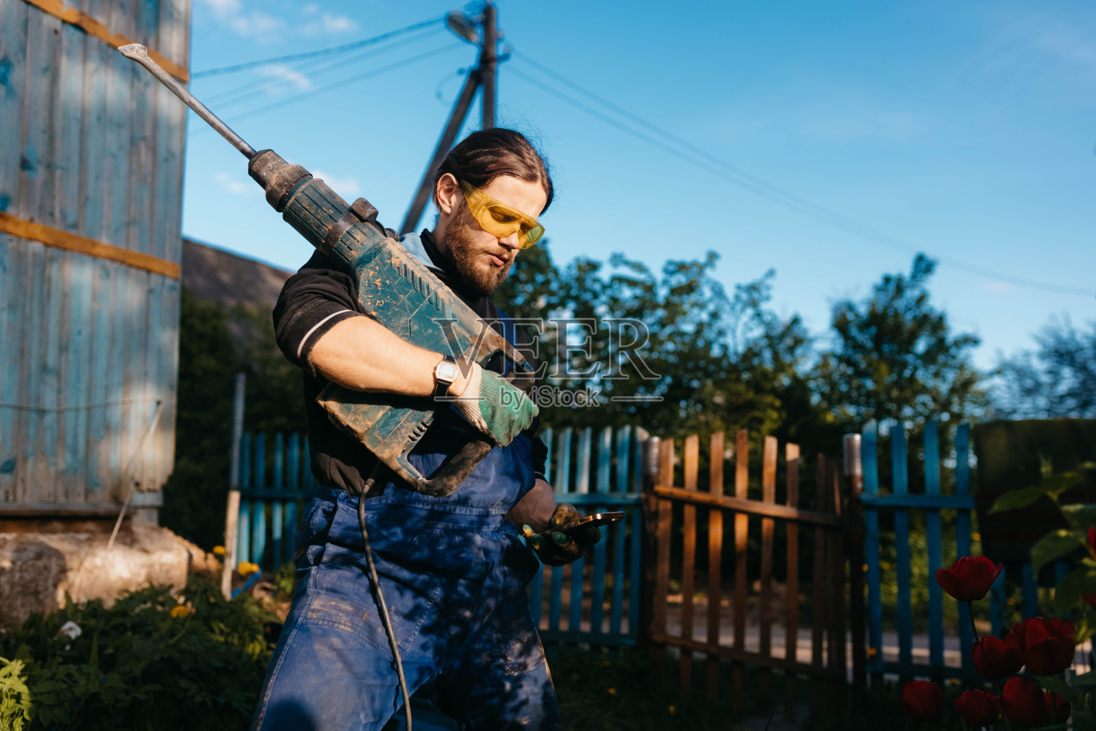 夏日里，一名戴着安全眼镜、拿着锤子的男工人在乡间别墅里。照片摄影图片