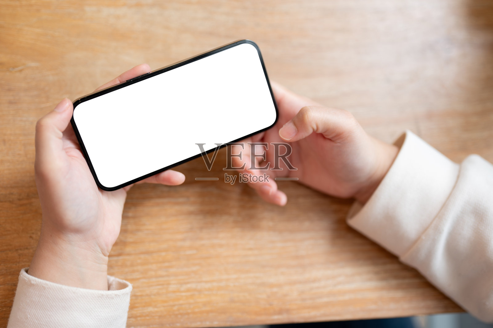 一位女士在室内的桌子上使用智能手机，将智能手机放在水平位置。照片摄影图片