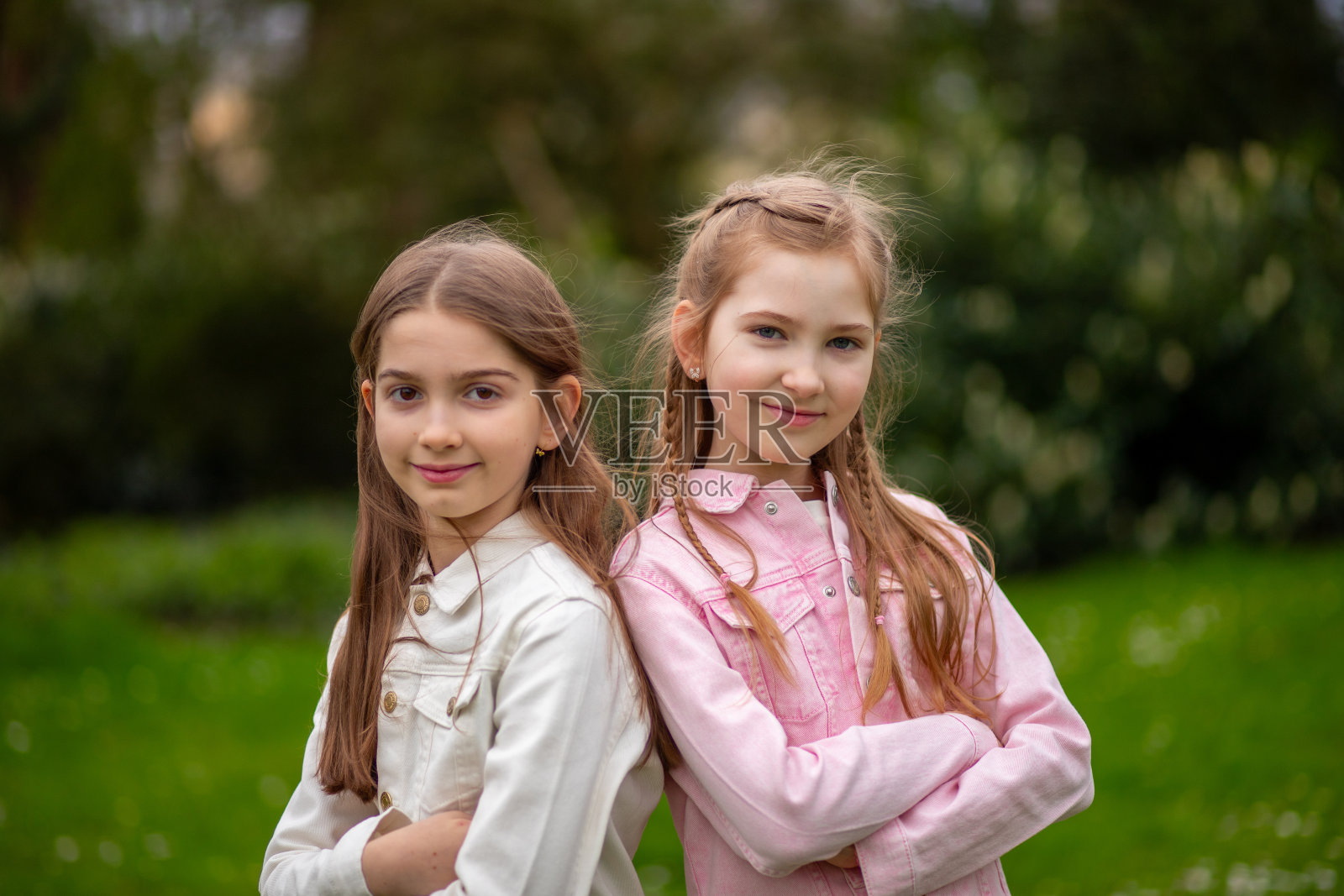 两个迷人的女孩穿着柔和的衣服，在绿色的春天公园里摆姿势。照片摄影图片