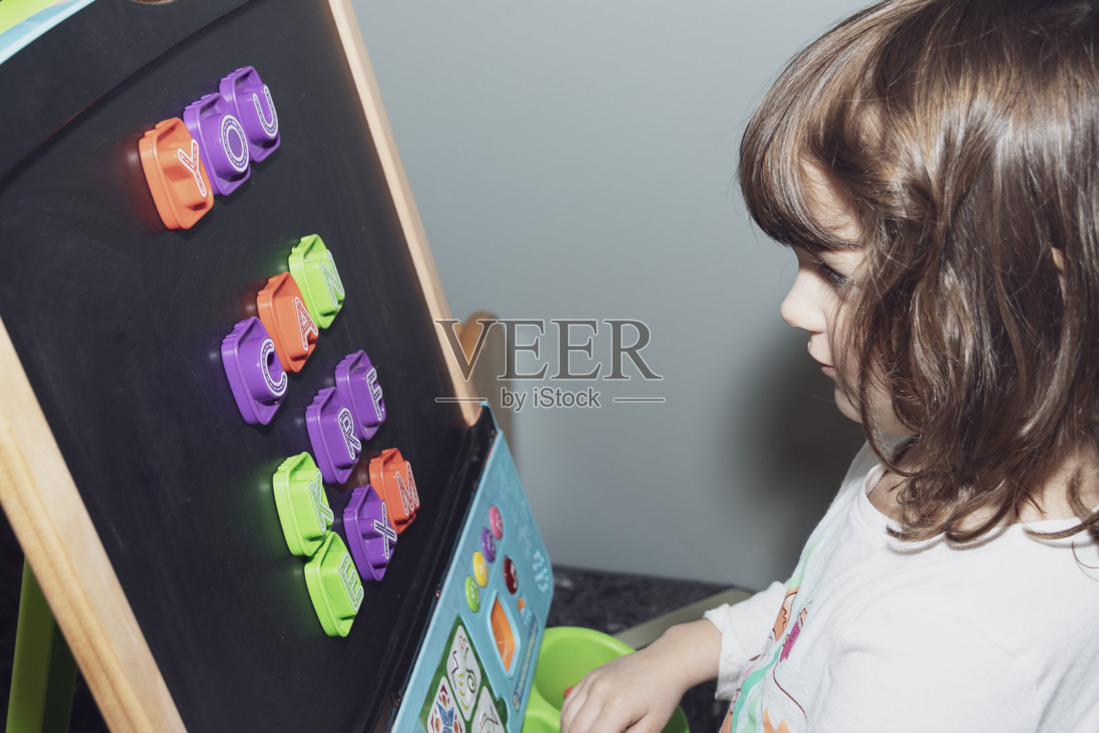 蹒跚学步的小女孩在家里的磁性画架上学习字母。照片摄影图片