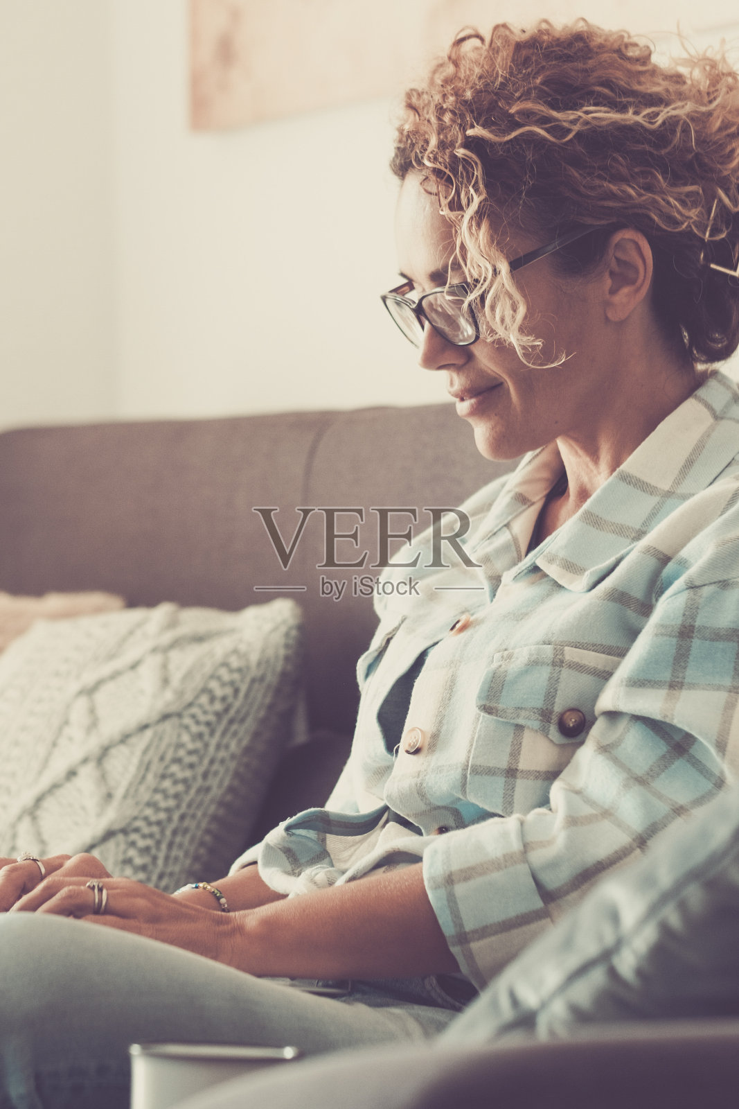 安详的成熟女子在沙发上使用笔记本电脑微笑着放松舒适的室内家居休闲活动。快乐的女性在有连接的电脑上上网。现代住宅生活方式照片摄影图片