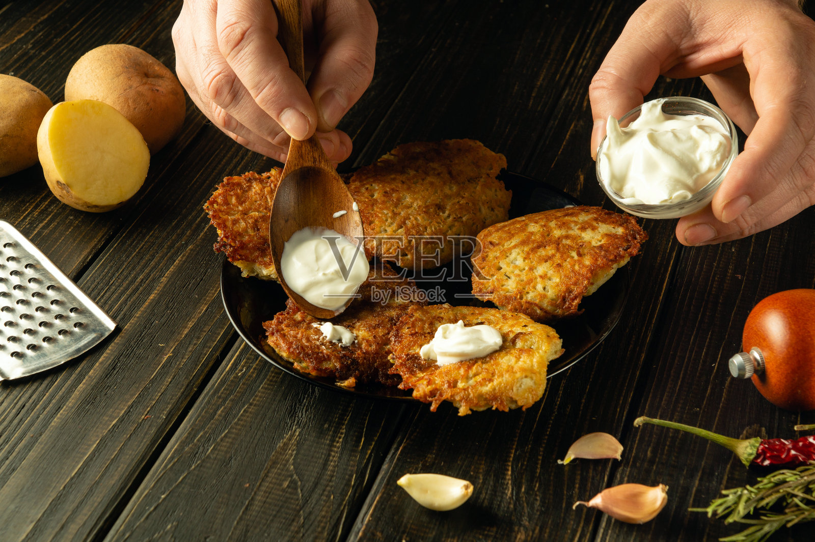 厨师用勺子往煎土豆煎饼里加酸奶油的特写镜头。在酒店或餐厅准备美味食物的概念照片摄影图片