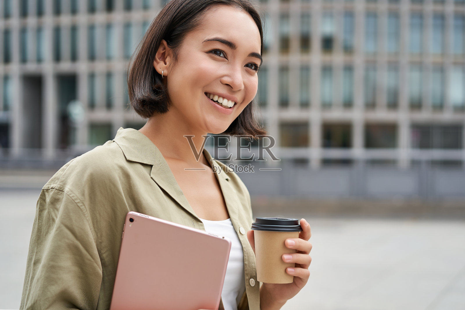 快乐的亚洲女孩的肖像，拿着平板电脑和咖啡，带着满意的微笑走在街上照片摄影图片