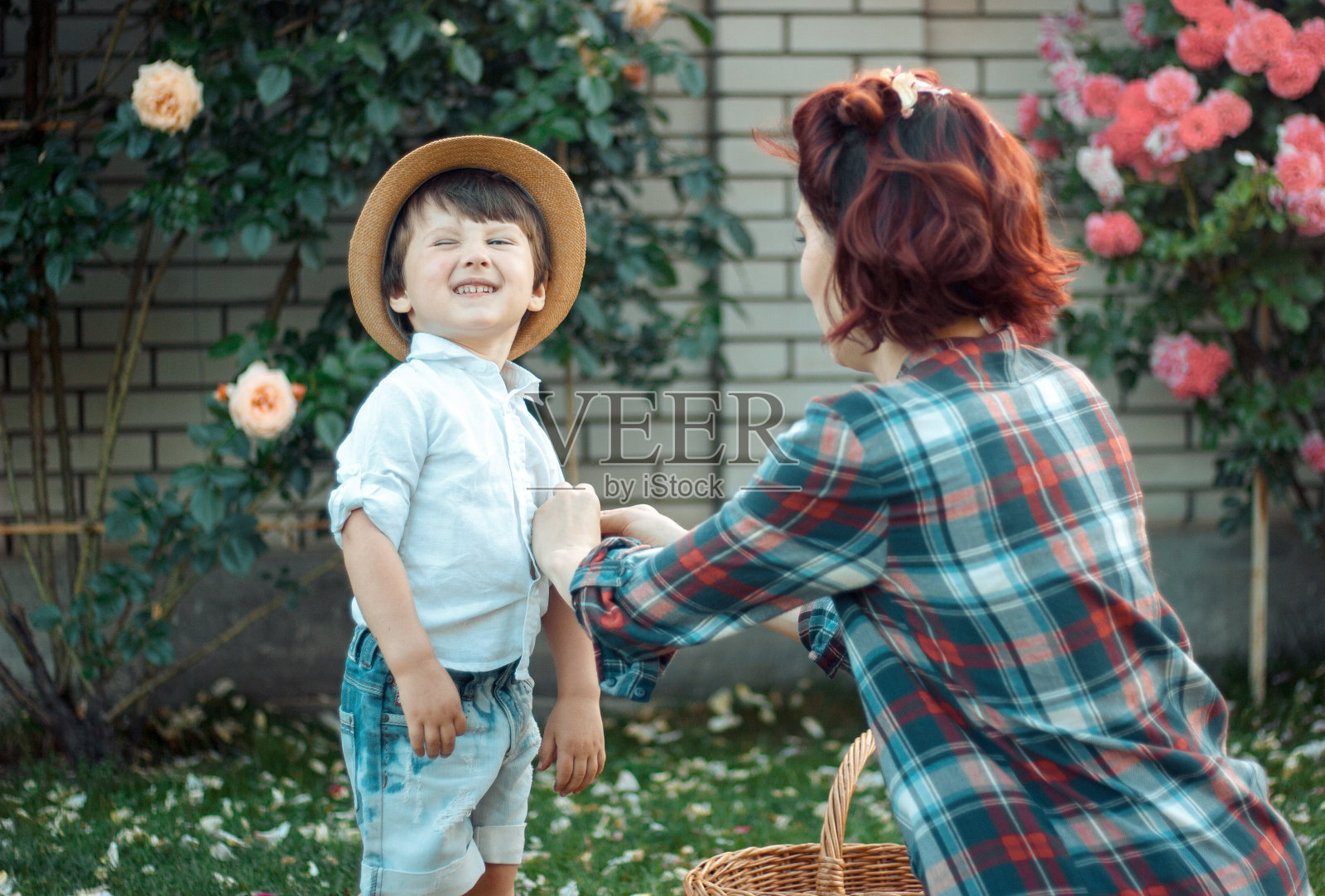 年轻的父母——穿着格子衬衫和牛仔裤的爸爸、妈妈和儿子，正坐在花园里开着玫瑰花野餐照片摄影图片
