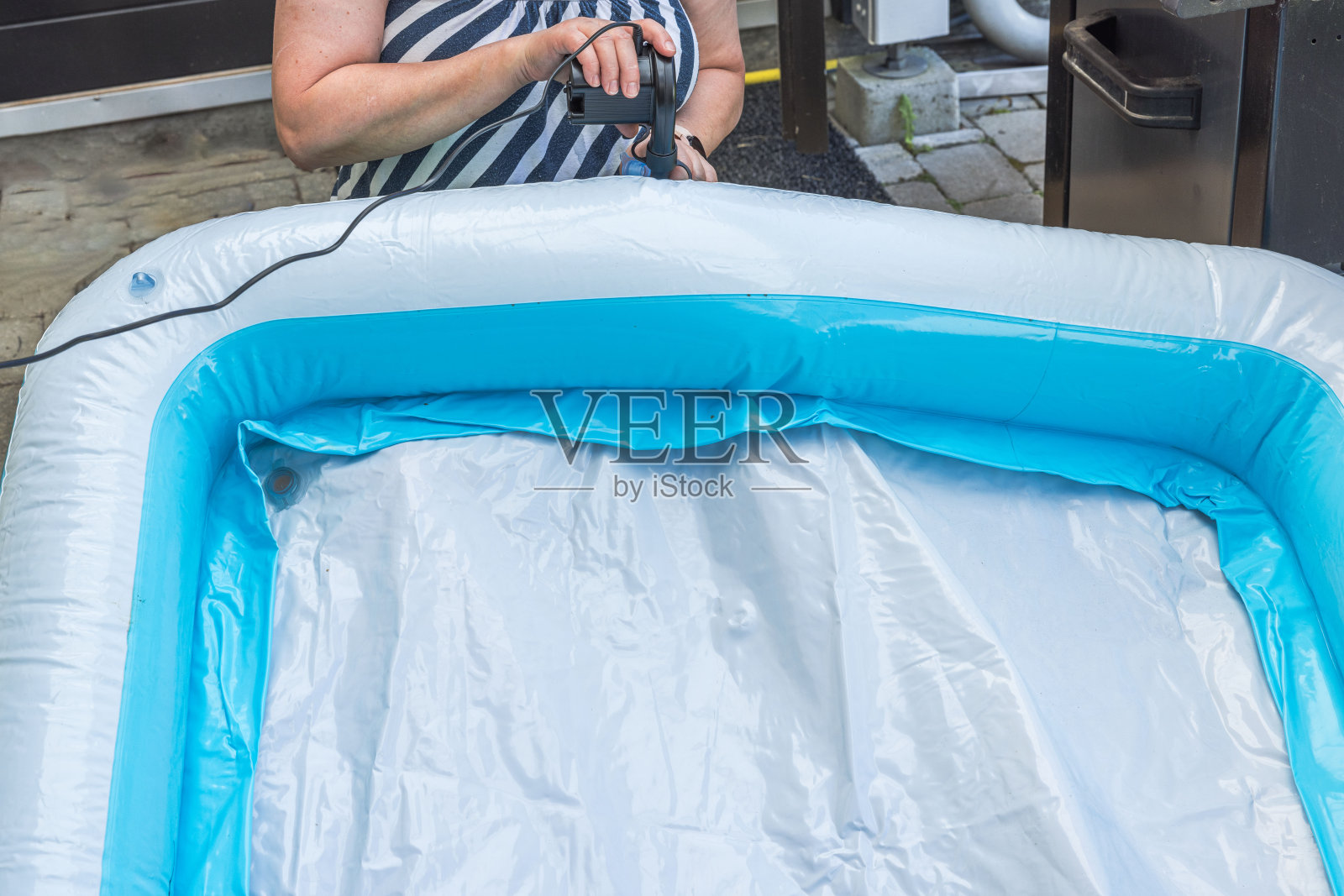 妇女用电动泵给儿童充气池充气的特写镜头。照片摄影图片