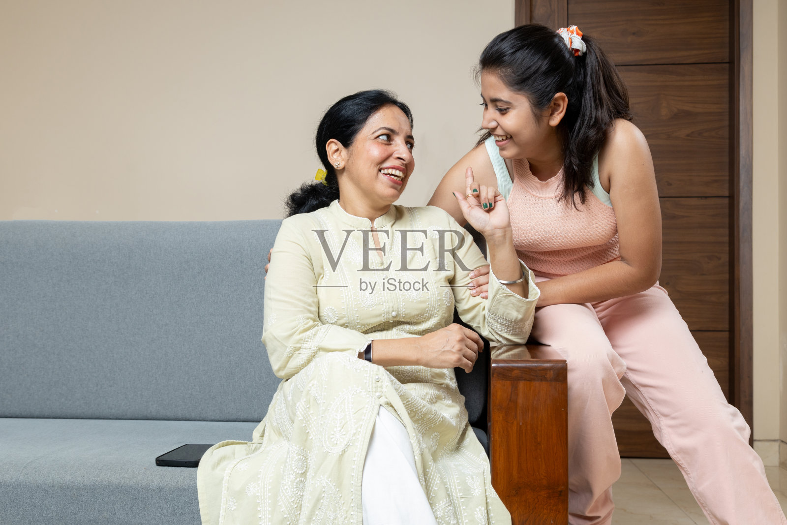 印度母亲和十几岁的女儿坐在家里的沙发上看着镜头，快乐的年轻女孩在客厅拥抱母亲，偷拍时刻照片摄影图片