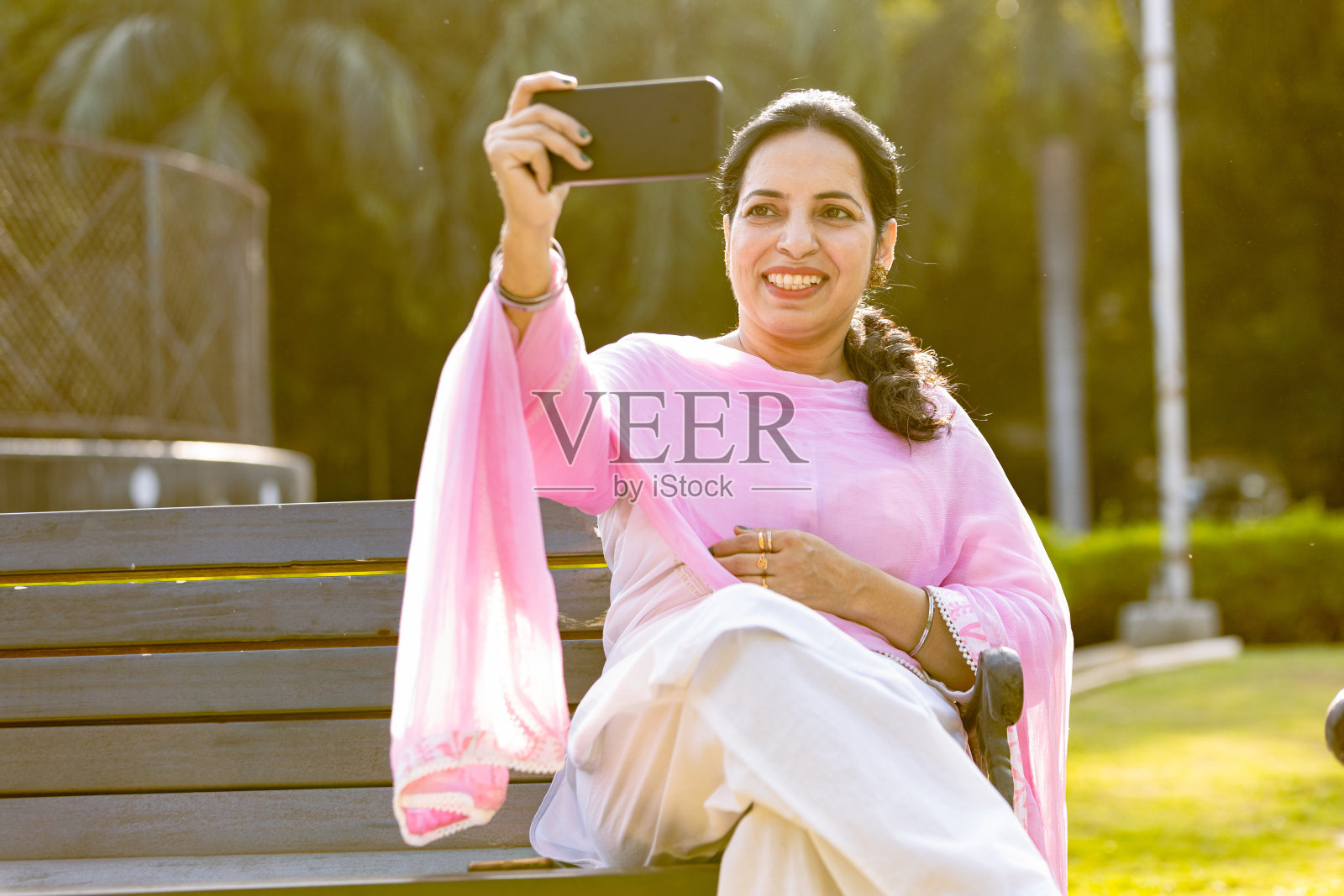 快乐的印度女人坐在户外公园用手机自拍照片摄影图片