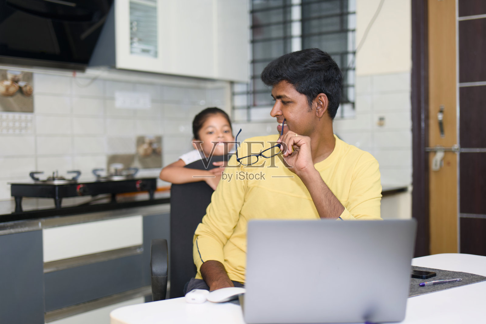 一位充满爱心的印度父亲耐心地帮助他的小女儿在厨房餐桌上使用笔记本电脑照片摄影图片