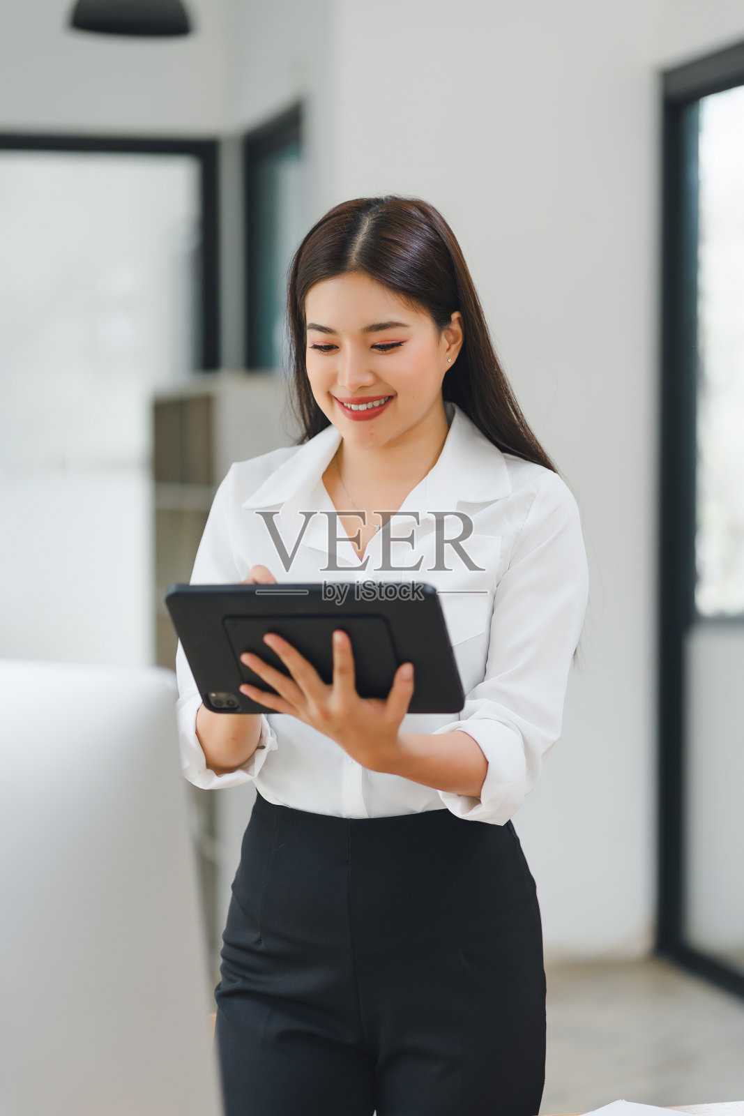 穿着白衬衫的微笑女商人在现代办公室里使用数码平板电脑。照片摄影图片