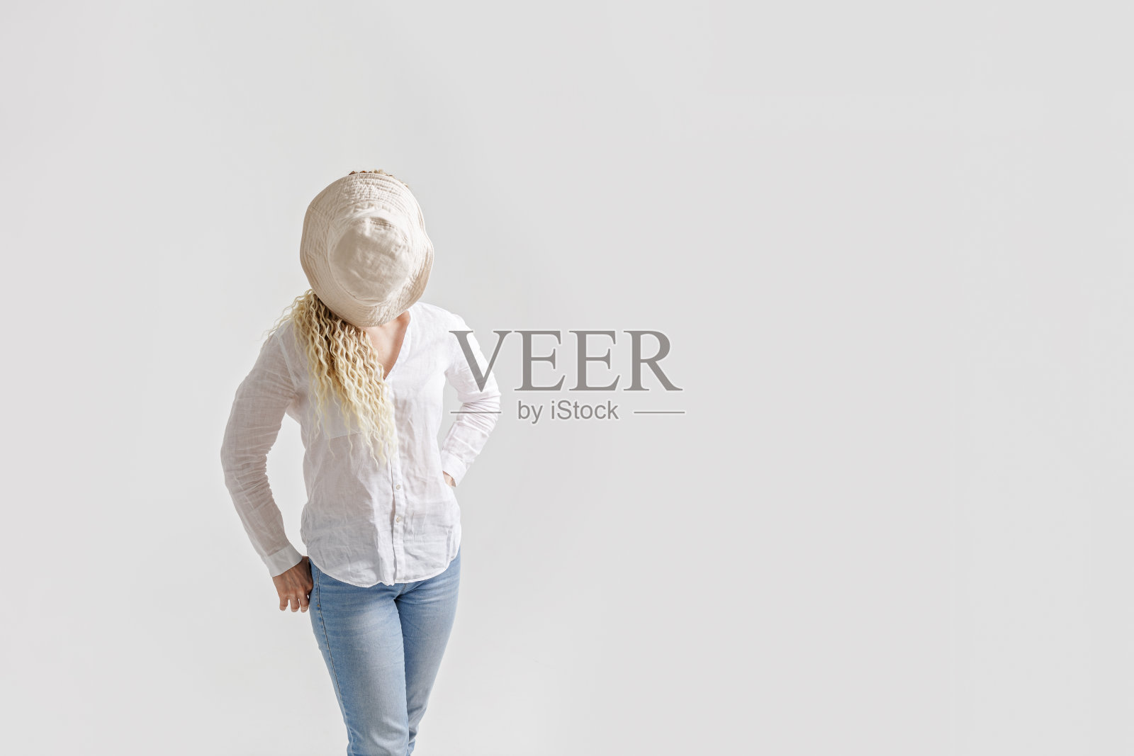 无脸潮流概念，女人把头藏在太阳帽里，浅白色背景，复制空间。年轻的女性，留着长长的脏辫，穿着白衬衫和牛仔裤。创意夏季视觉。假期的概念照片摄影图片
