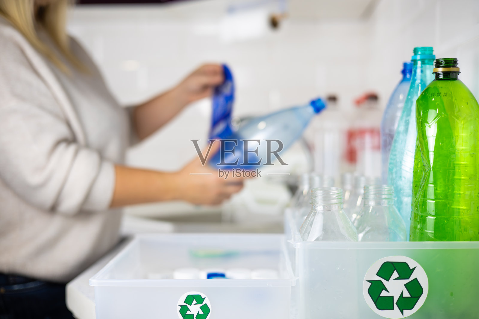 一名妇女在塑料瓶被送去回收前取下标签。一名妇女在自家厨房里把塑料按类型分类，以便回收利用。生态行动主义的概念，关爱自然。照片摄影图片