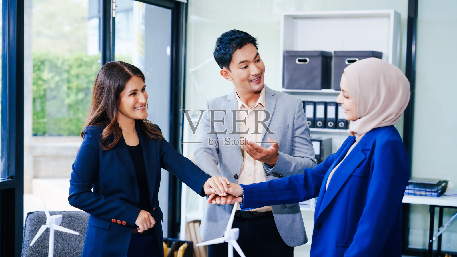三位商人围坐在一张桌子前，手拉着手象征团结。在一名亚洲中年男女的带领下，他们为一个更清洁、更节能的未来制定了可持续的解决方案。照片摄影图片