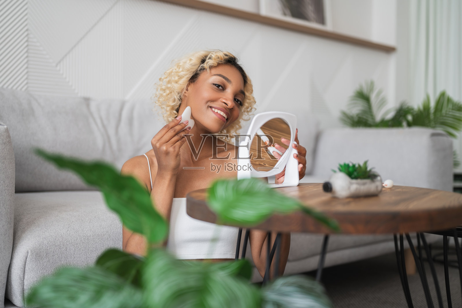 美容习惯。迷人的黑人女性用刮刀按摩脸部照片摄影图片