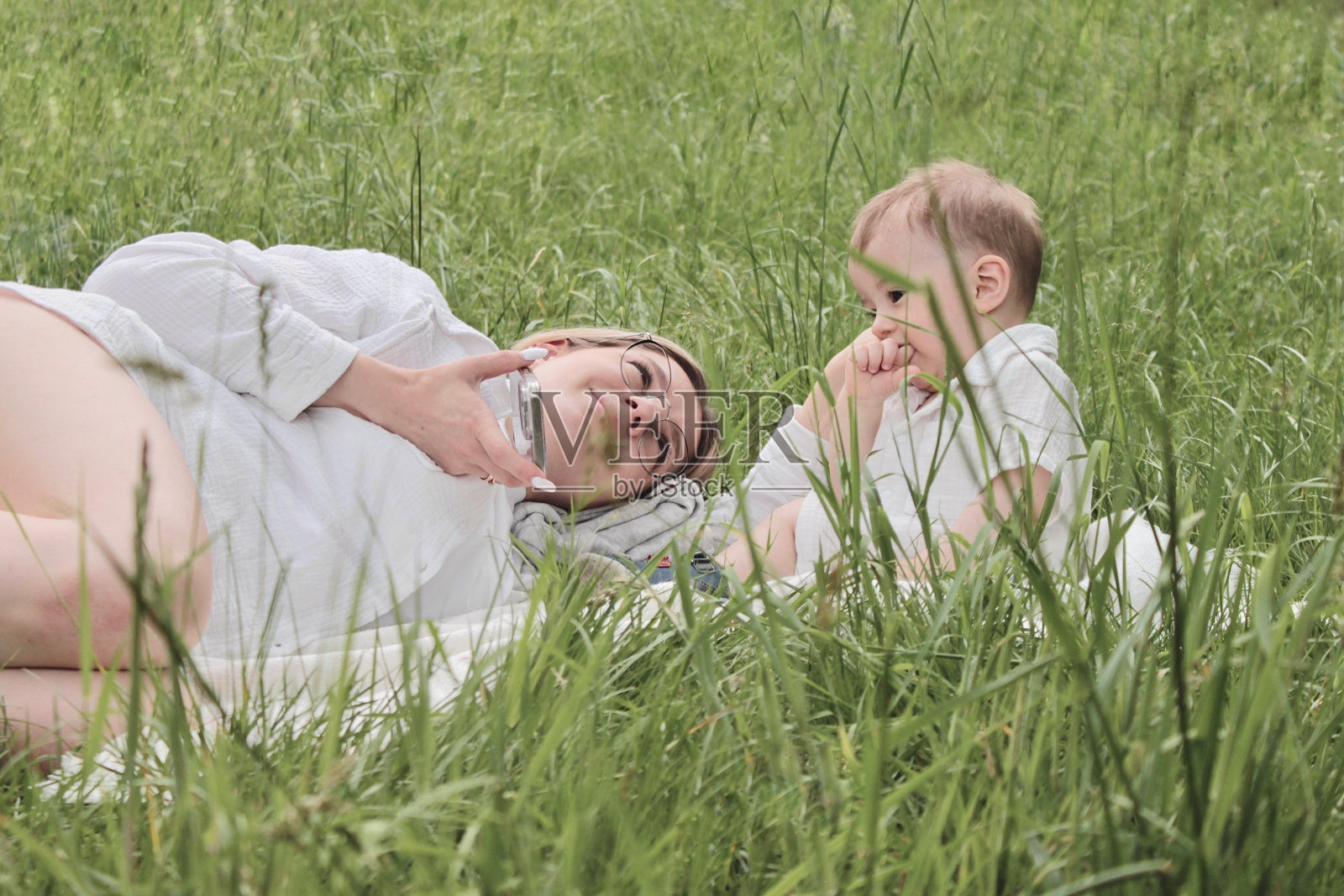 晴朗的天气里，一位年轻的母亲带着一个小男孩在公园的草地上休息照片摄影图片