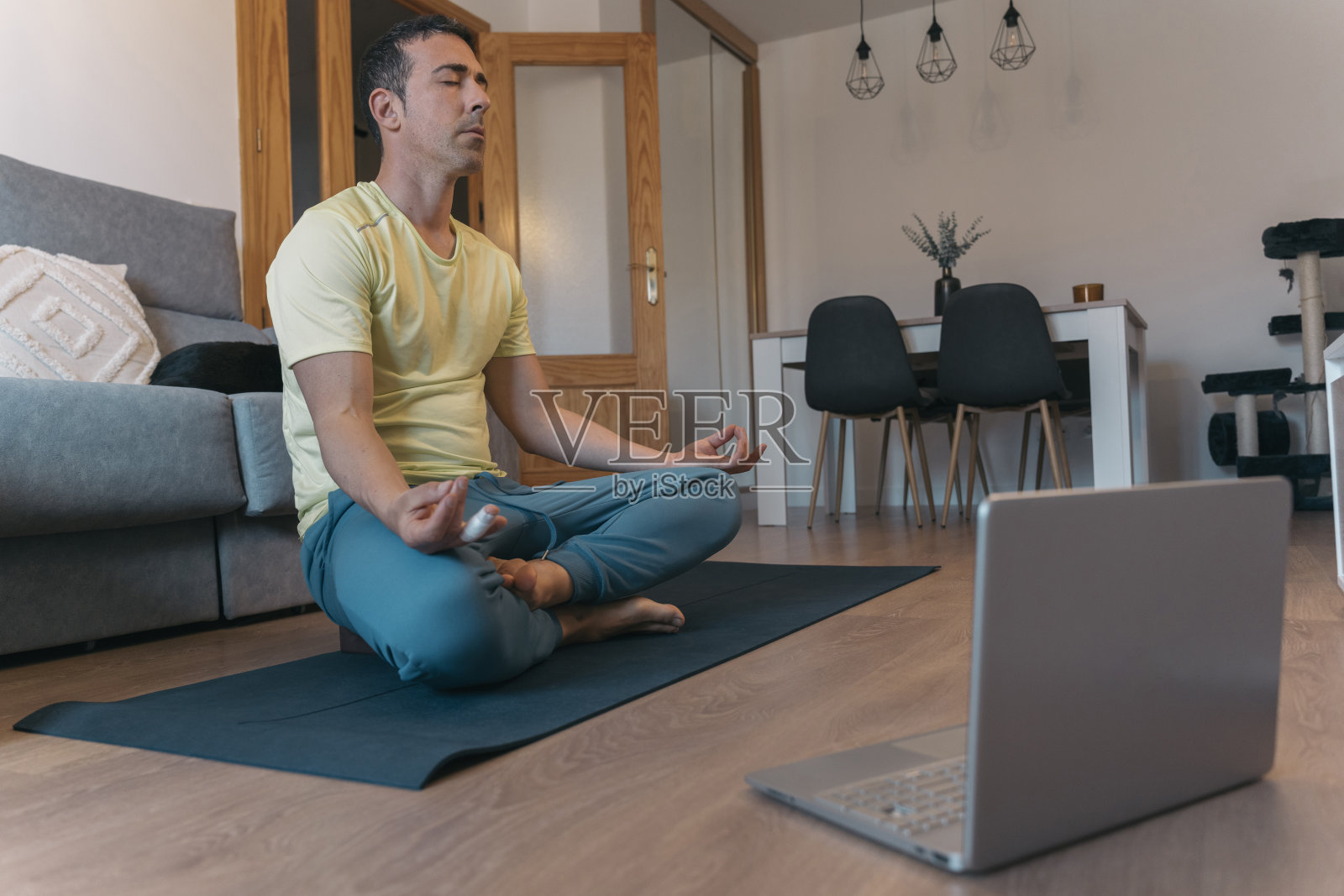 年轻人在客厅的瑜伽垫上练习正念。在宁静的客厅里，一个姿势端庄的年轻人闭着眼睛坐在瑜伽垫上冥想。照片摄影图片