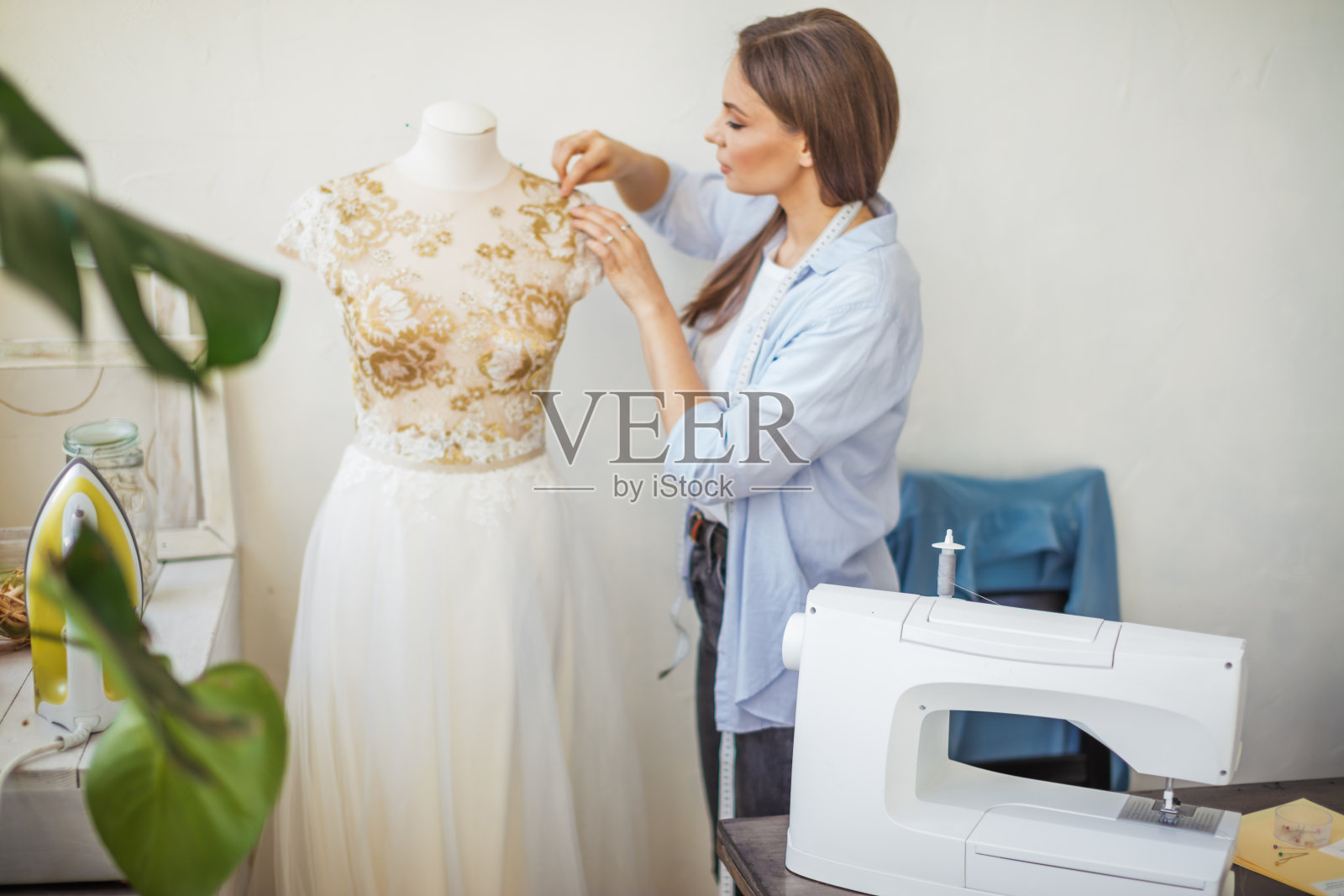 美丽的女裁缝正在她的工作室里和婚纱模特一起工作照片摄影图片