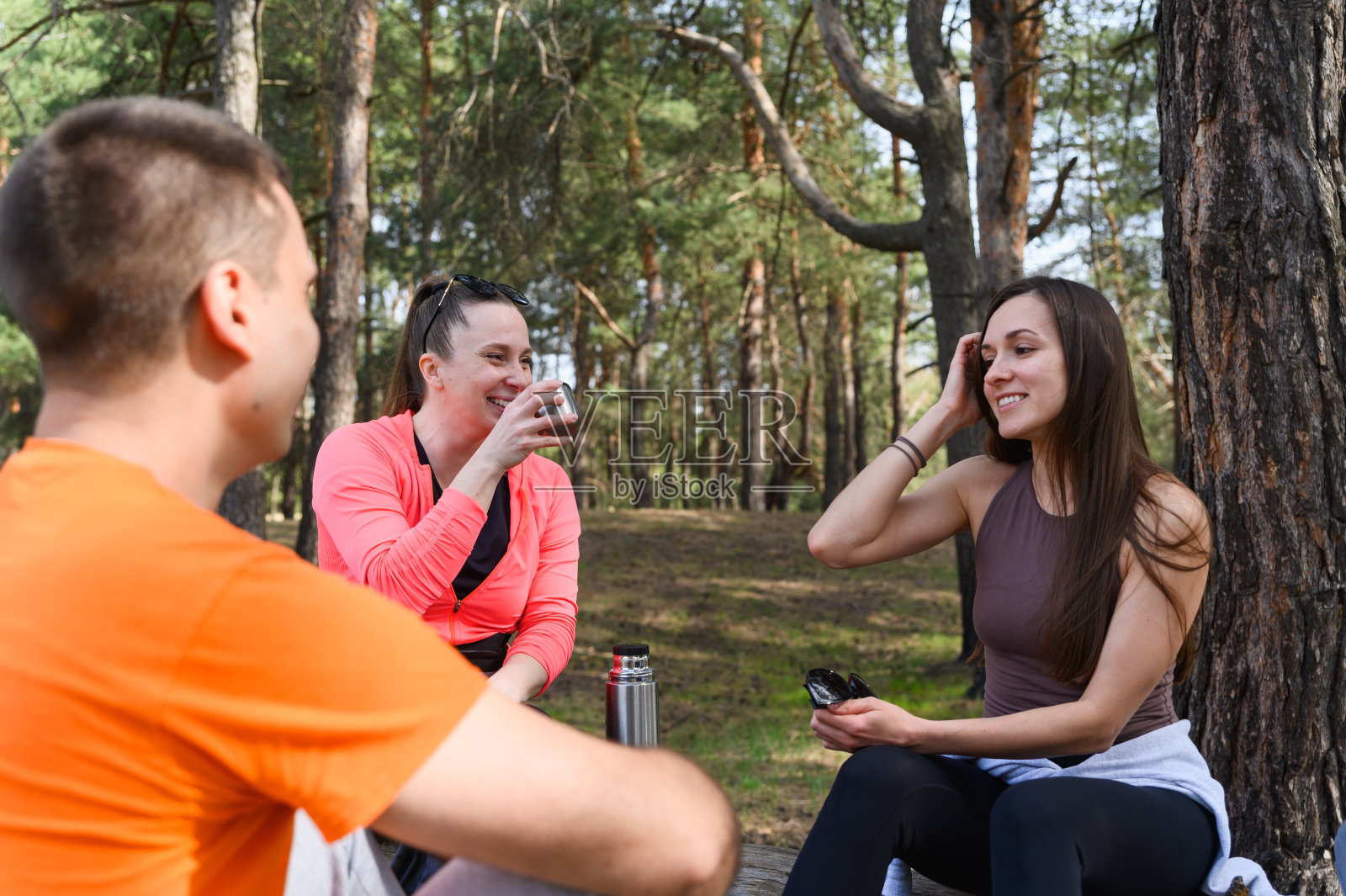 三个朋友在一次徒步旅行中在一根倒下的原木上休息。照片摄影图片