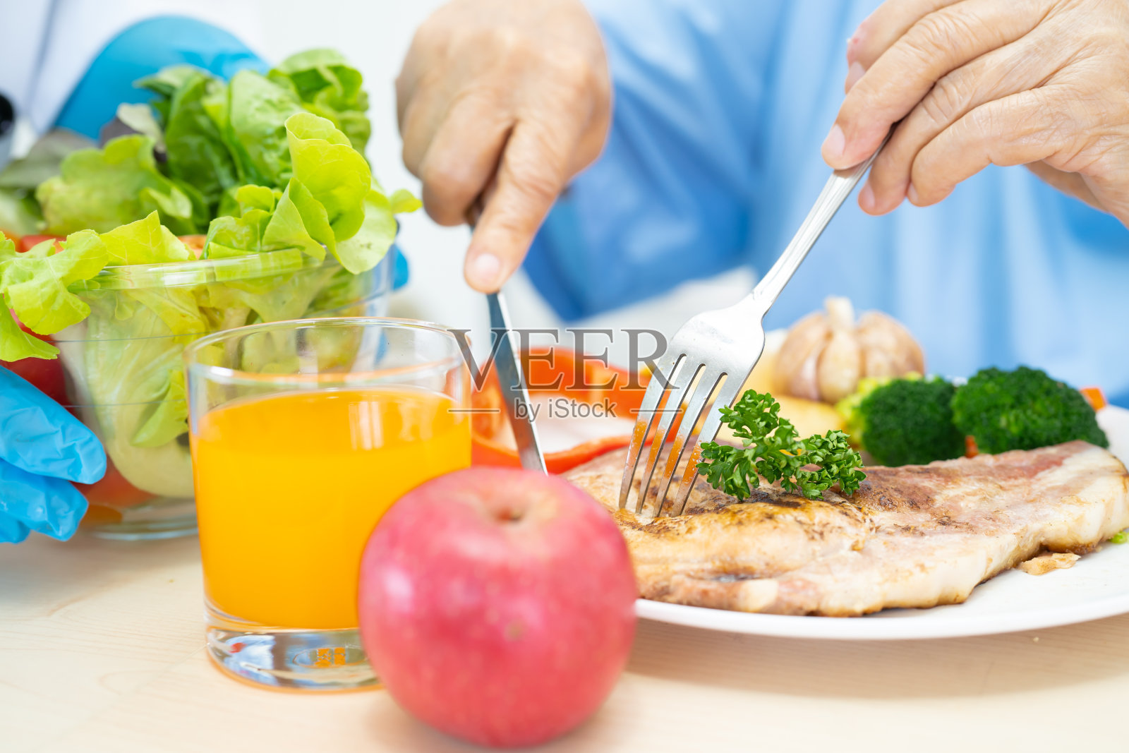 亚洲老年妇女病人坐在医院的床上饿着肚子吃着鲑鱼牛排早餐和蔬菜健康食品。照片摄影图片