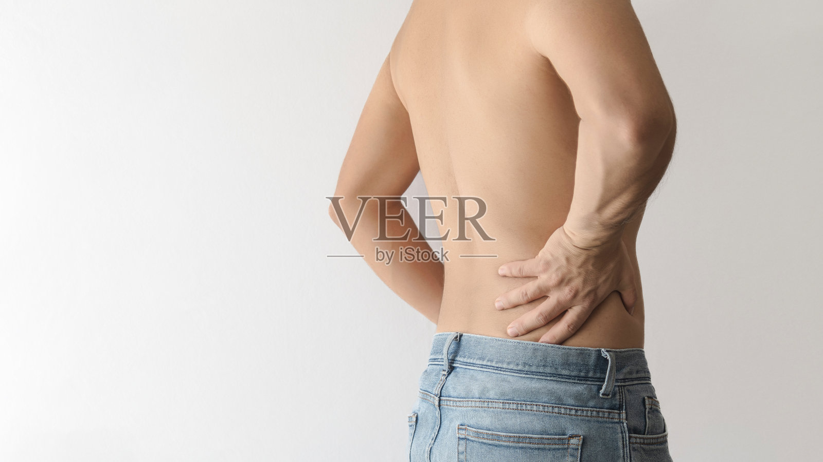 赤裸上身的男子因疼痛而转身并用手触摸下背部，白色背景左侧留出文字空间照片摄影图片