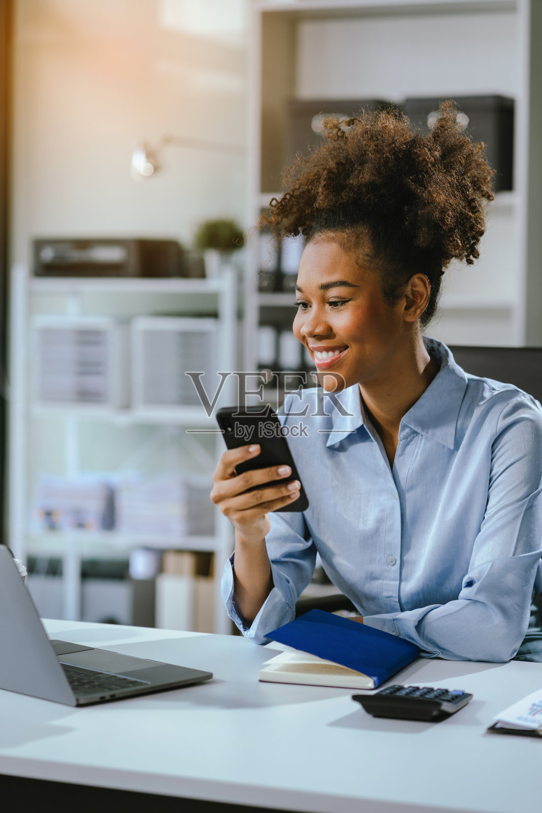 快乐的黑人女商人在创意办公室里用智能手机玩社交游戏。照片摄影图片