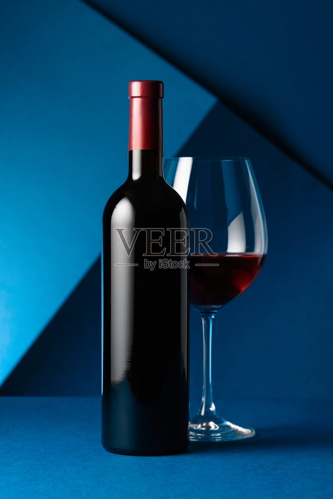 一瓶和一杯蓝色背景的红酒。照片摄影图片