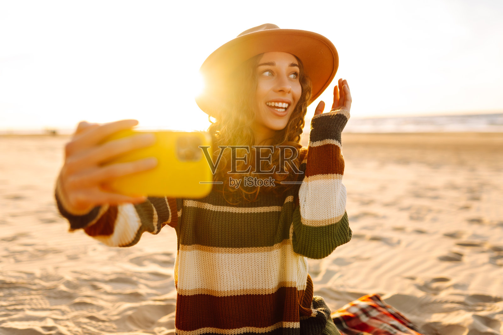 美丽的卷发女人在日落时在海边摆姿势。照片摄影图片