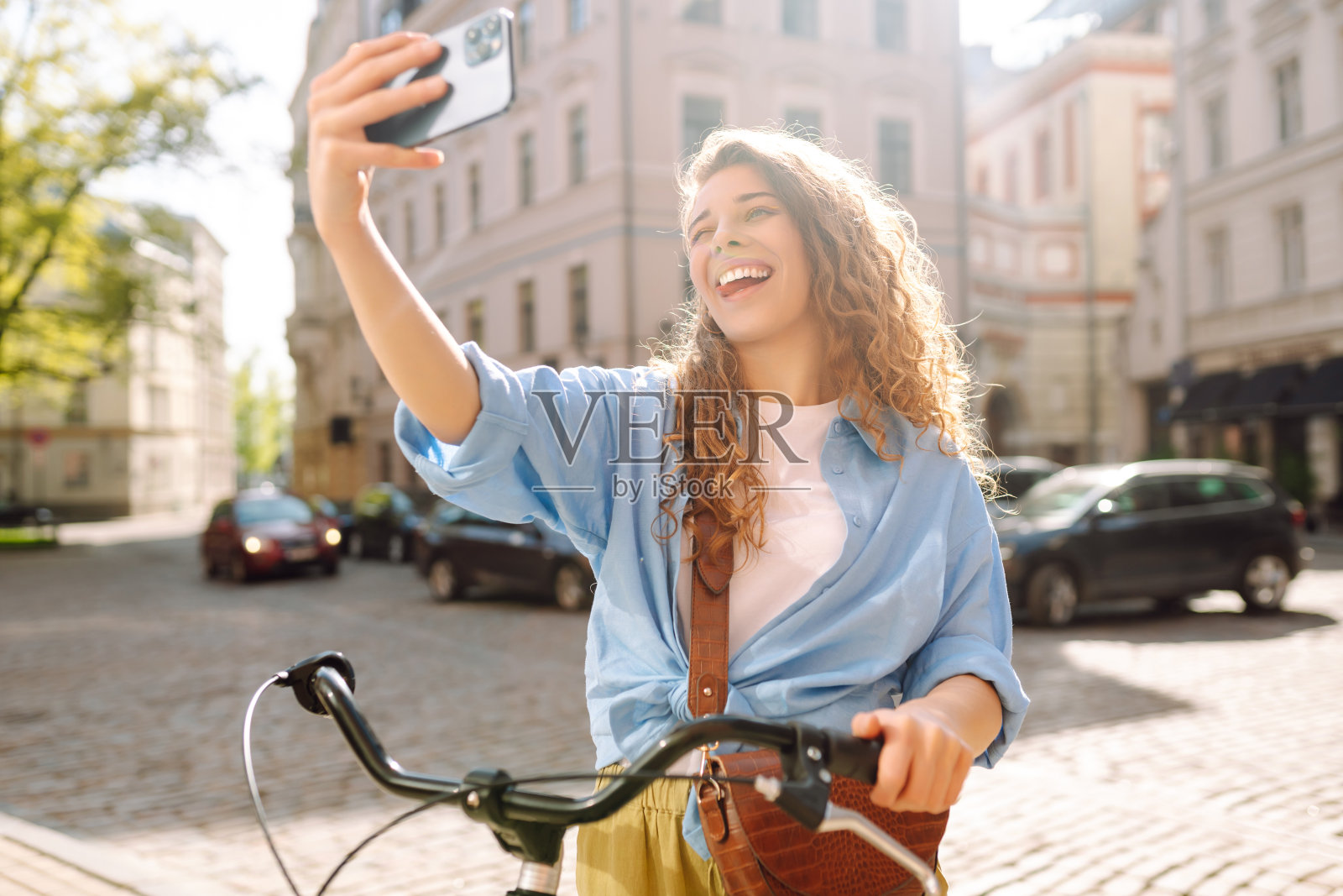 一名年轻女子在城市的户外街道边骑自行车边玩手机。照片摄影图片