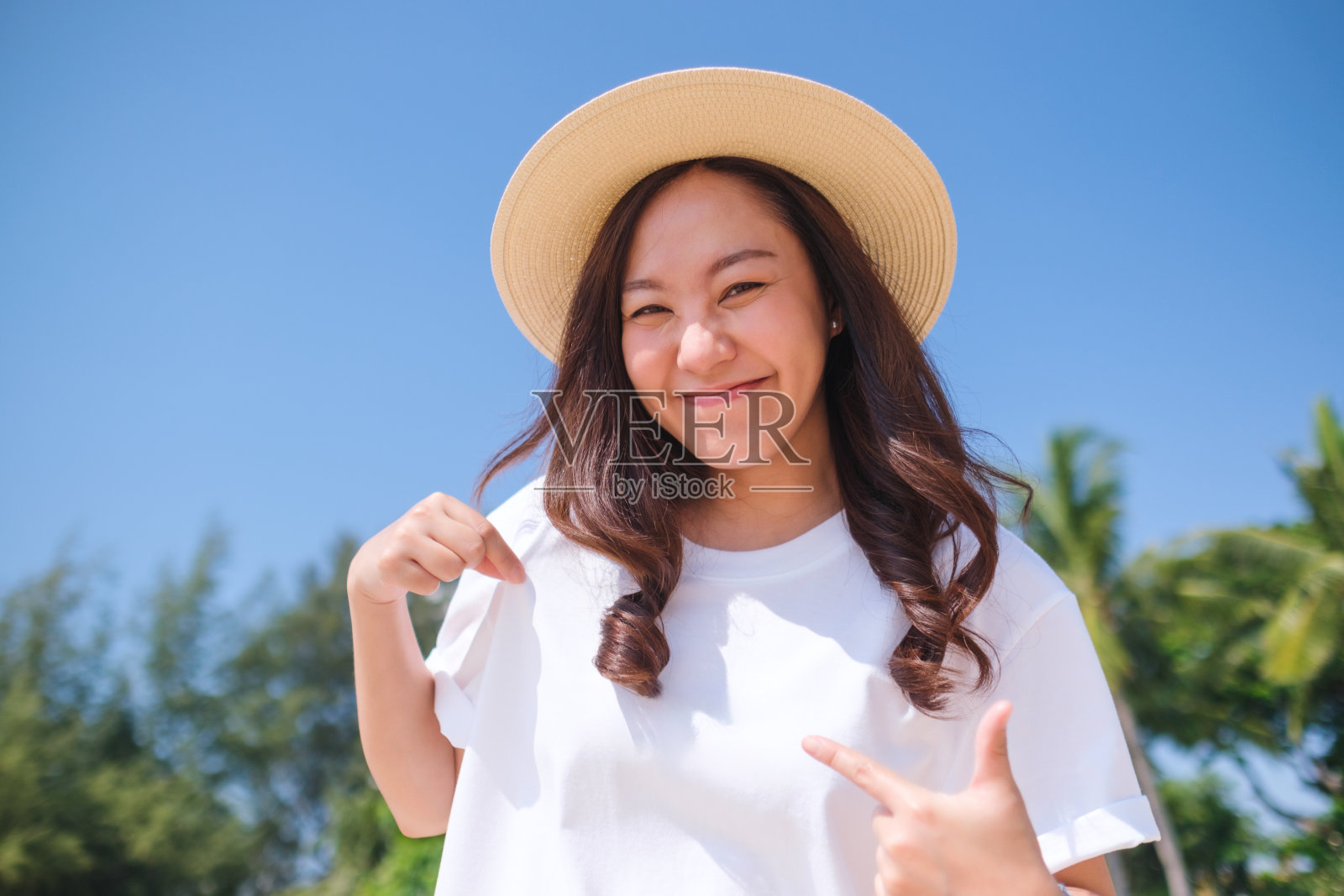 一名年轻女子指着一件蓝色天空背景的白色t恤照片摄影图片