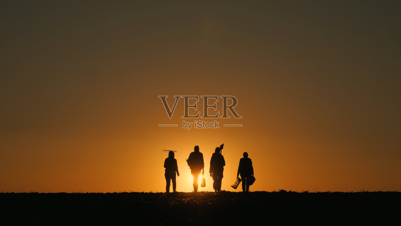 一户农民带着设备走过田地。夕阳下的剪影。后视图照片摄影图片