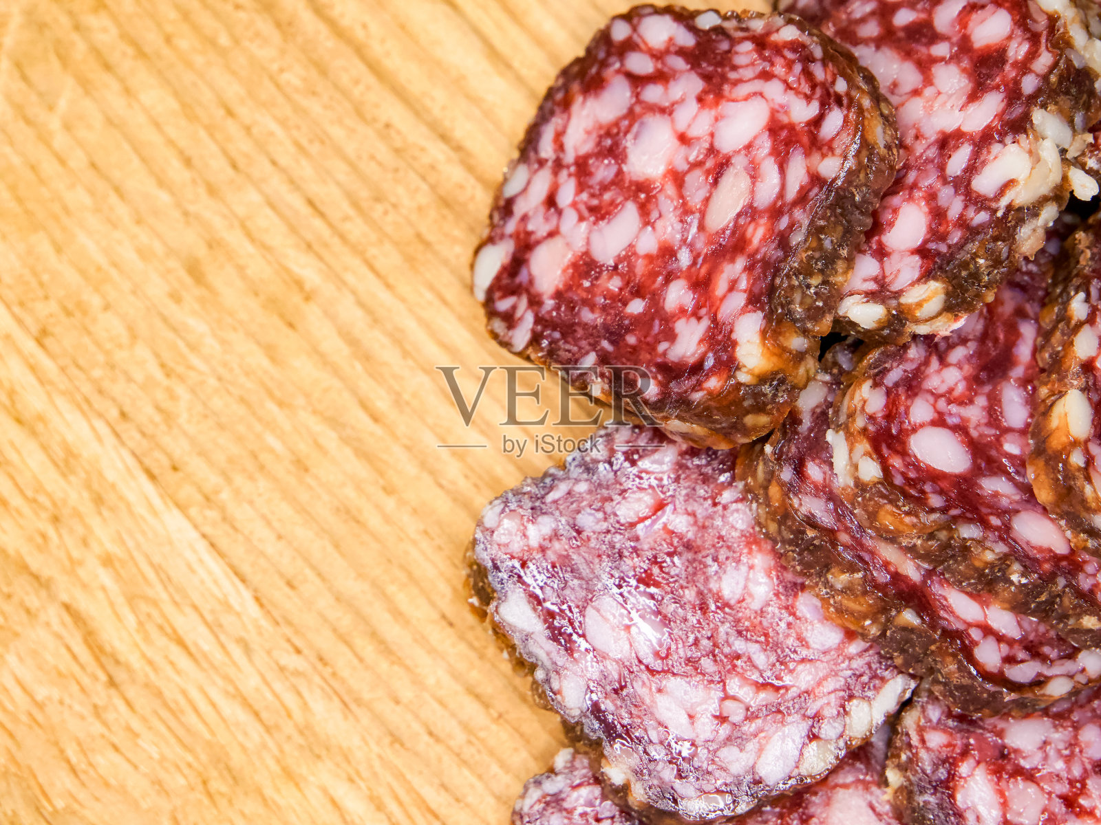 一张木桌的特写，上面放着一堆肉。肉是切片的，他是意大利腊肠。照片摄影图片