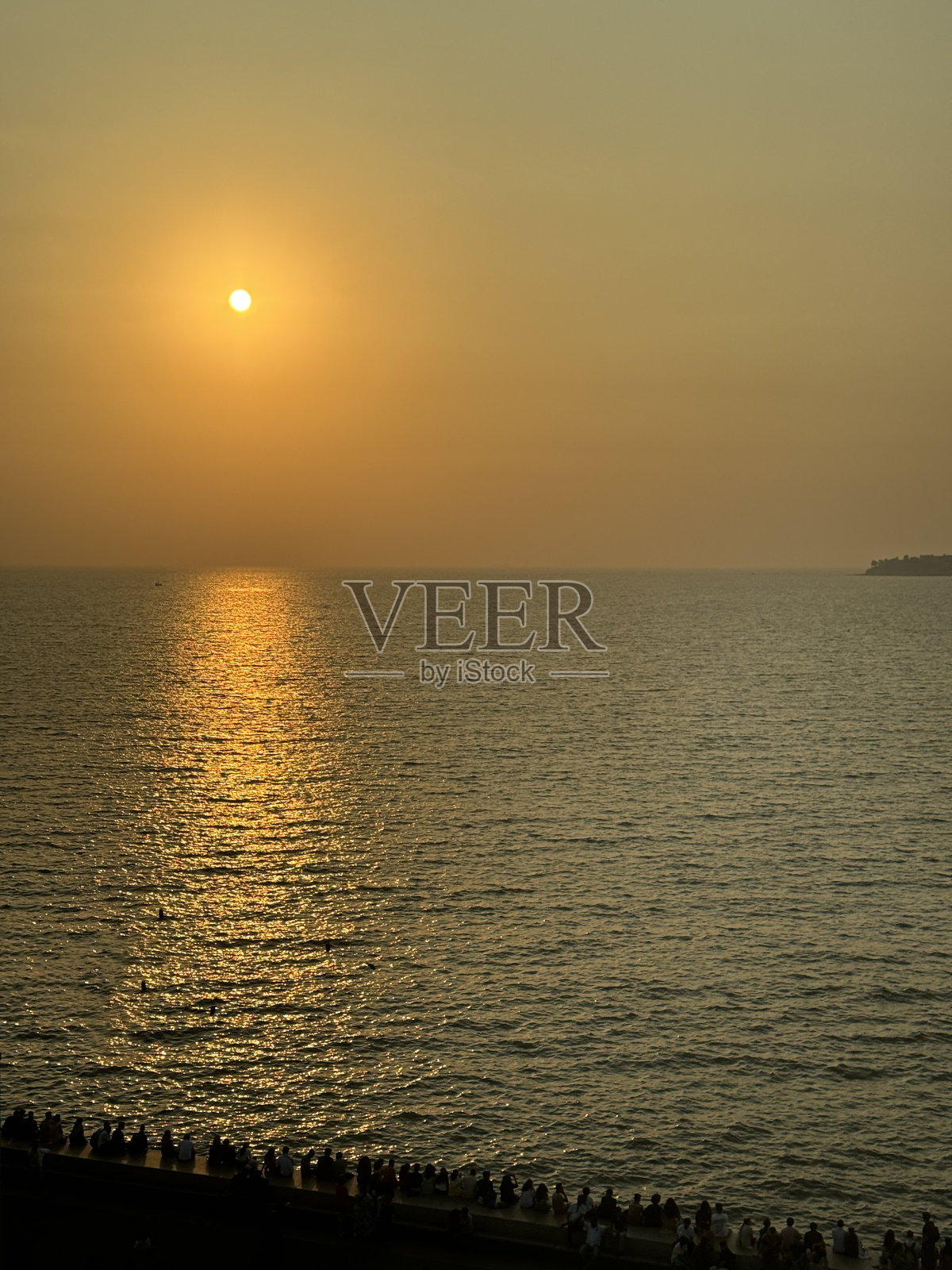 印度孟买，人群站在滨海大道海堤上观看日落，橙色天空照片摄影图片