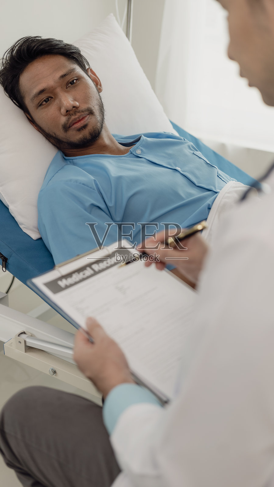 一名年轻男子躺在医院病房的床上和她年轻的印度医生交谈。医生检查病人的健康，医生治疗病人，病人住院照片摄影图片