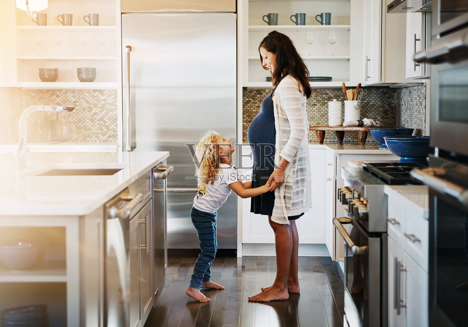 跳舞，音乐和怀孕的母亲带着孩子在厨房听专辑，收音机或播放列表。微笑，爱和妈妈玩得开心，和女孩一起移动，在家里为母亲们唱歌。照片摄影图片