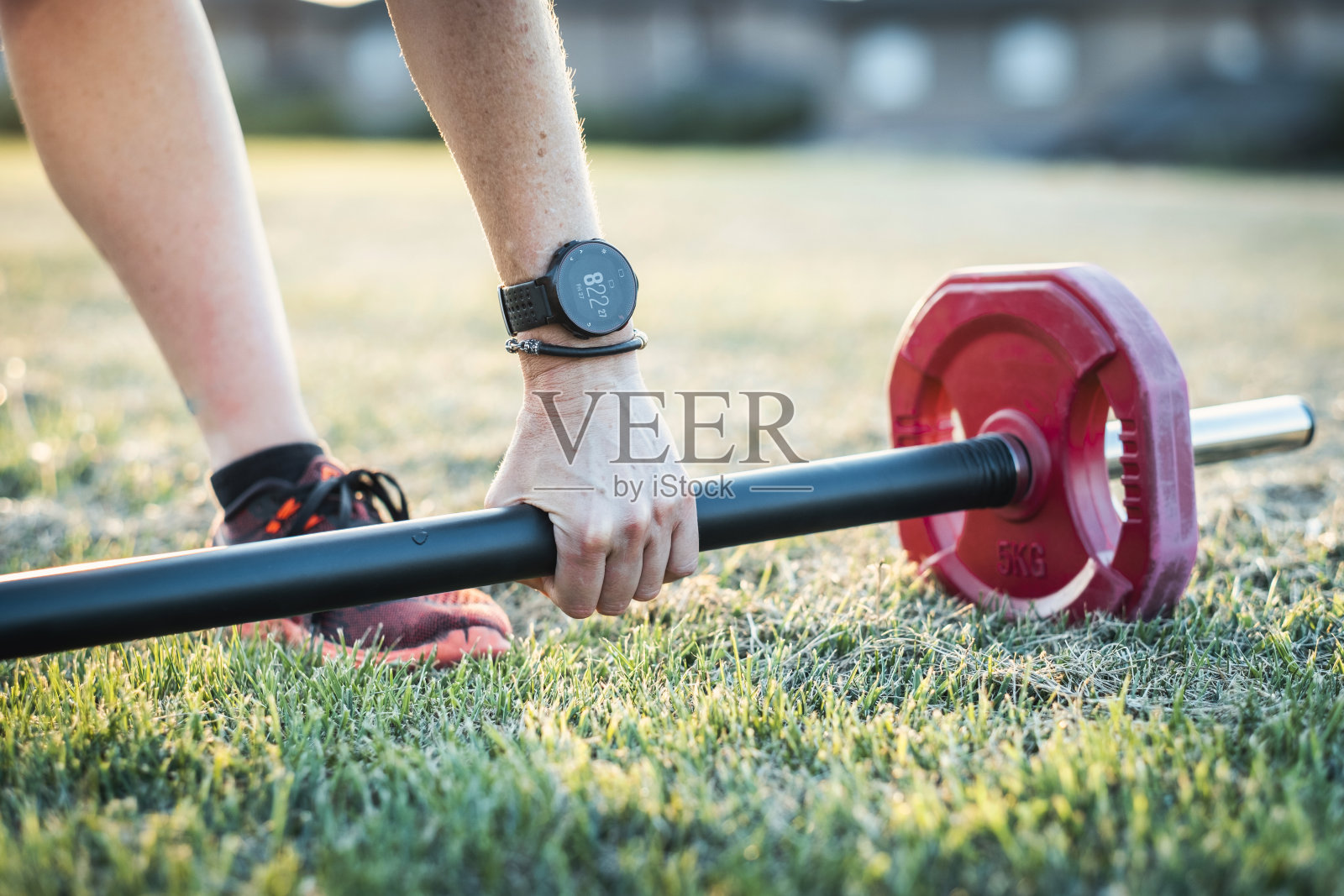 一个人在草地上举着一根红色的杠铃。照片摄影图片