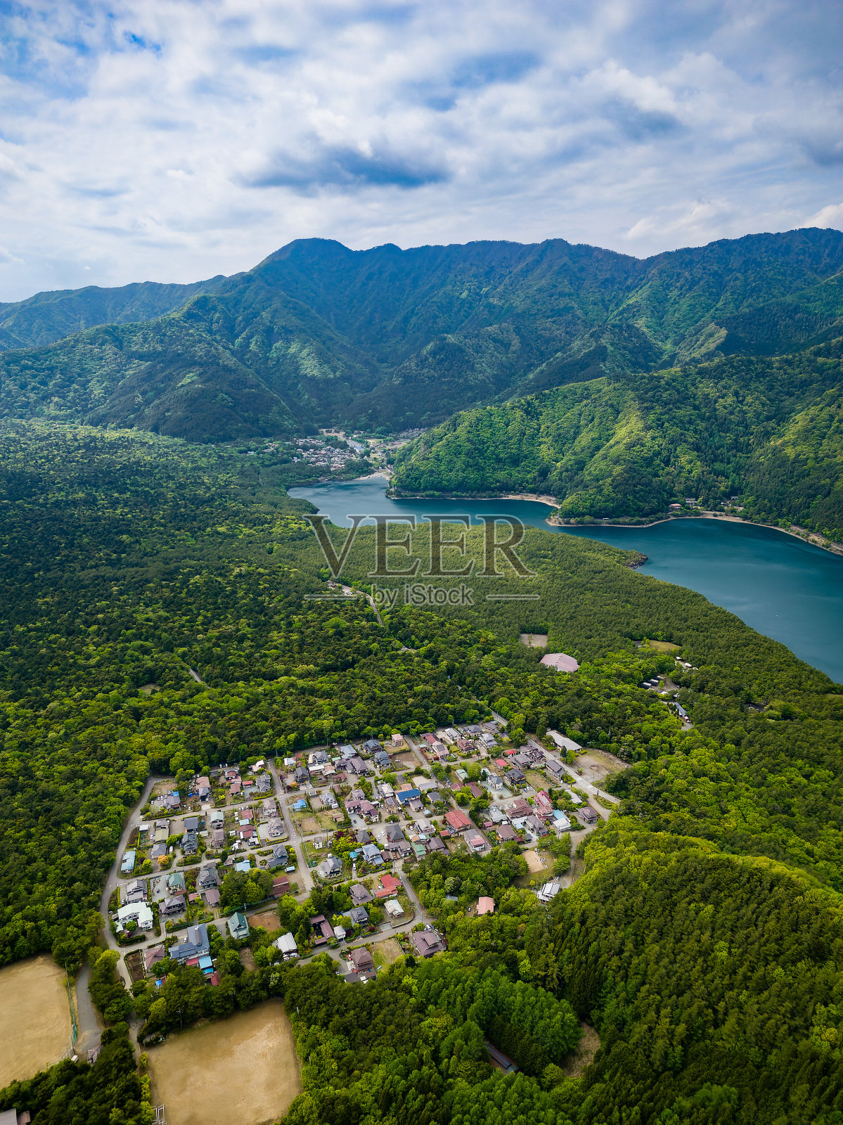 小村庄环绕着茂密的森林和崎岖的山脉，旁边的湖(Saiko，日本)照片摄影图片