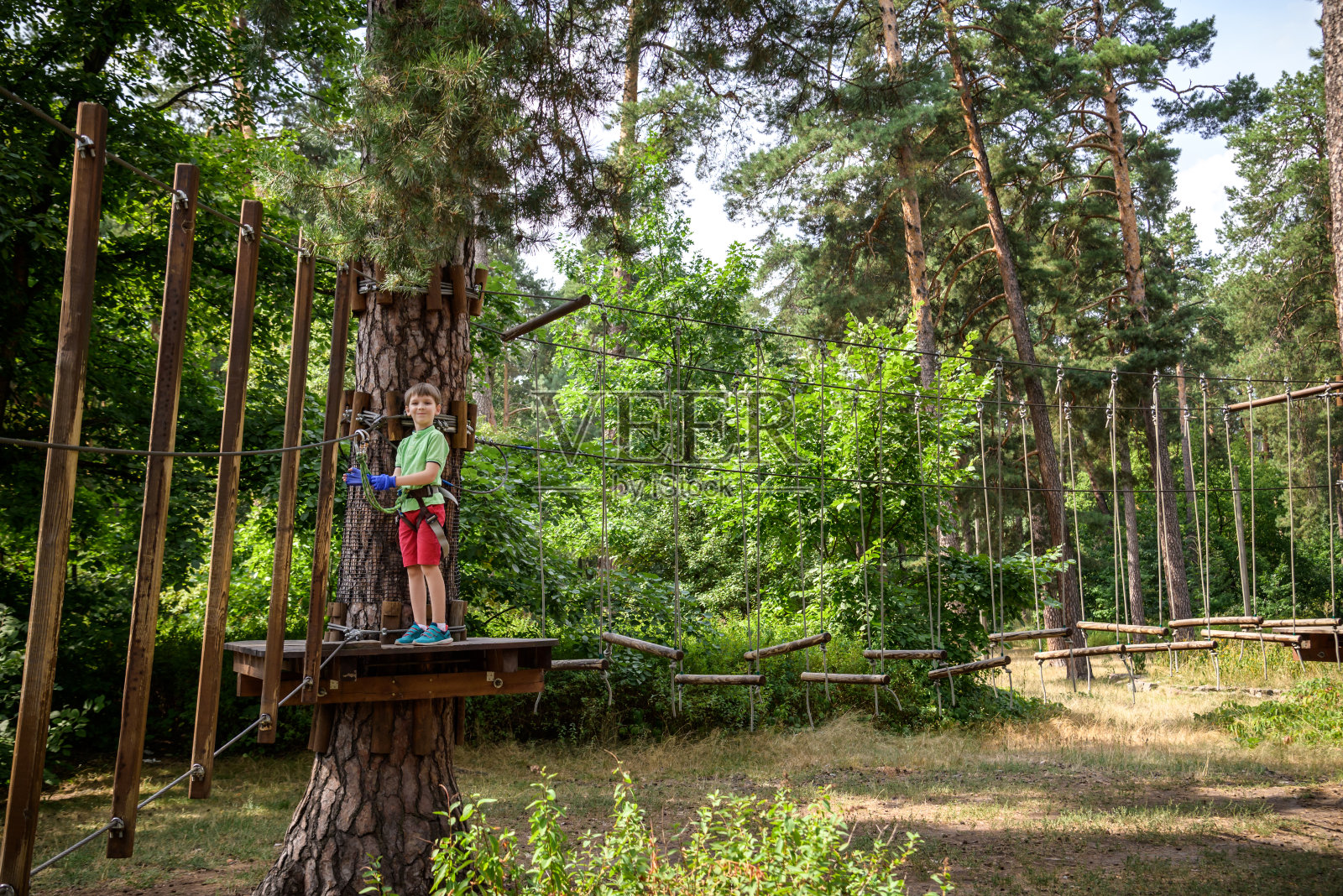 强壮兴奋的小男孩在户外绳索公园玩耍。在温暖的阳光下，穿着休闲服和运动鞋的高加索孩子。积极的休闲时间与孩子的概念照片摄影图片