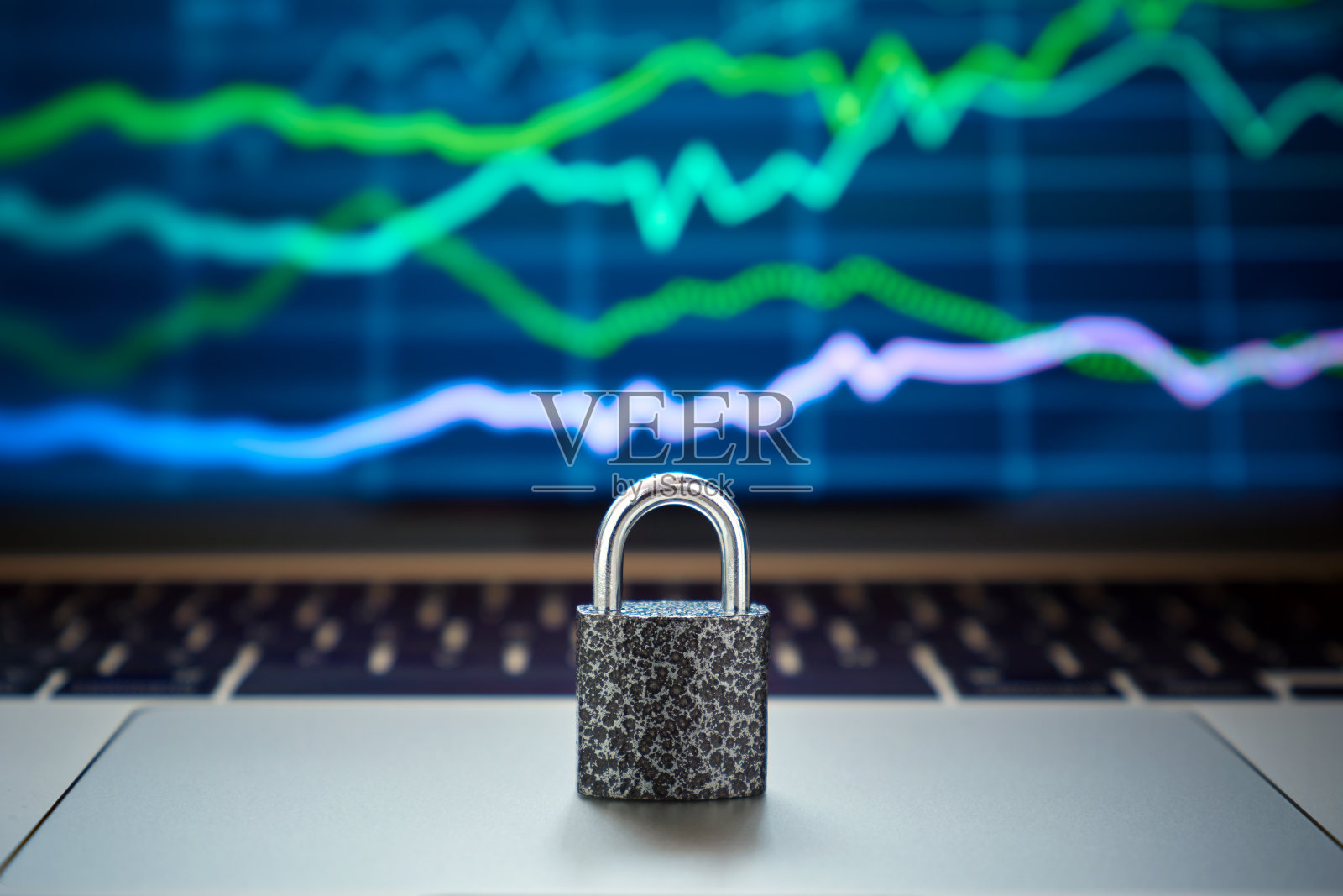 笔记本电脑上的金属锁的特写，背景是一个屏幕，上面是证券交易所的股票报价图表。照片摄影图片