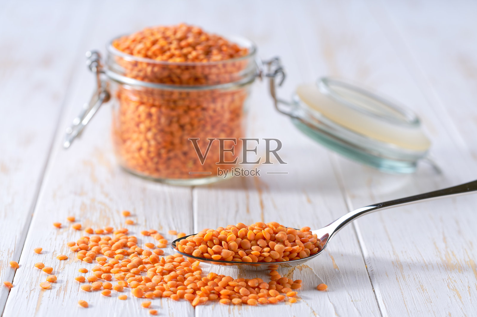 金属勺子上放着红色的生扁豆，放在一张浅色的桌子上，选择性地聚焦。照片摄影图片