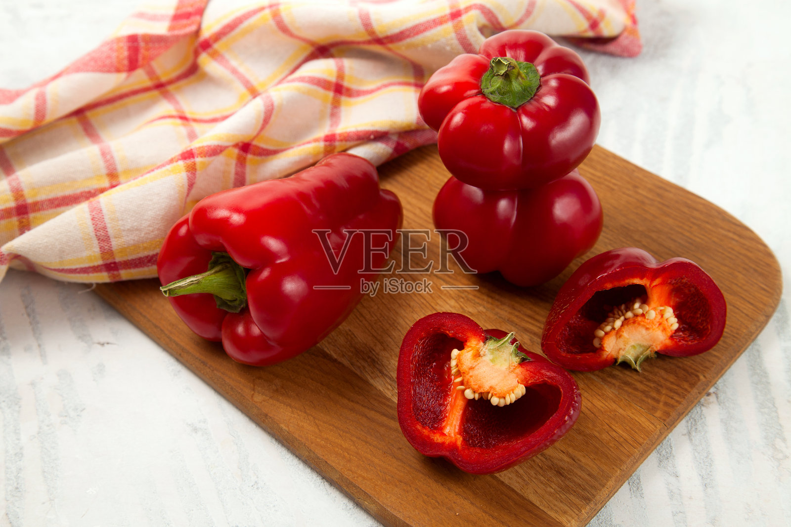 砧板上有几个完整的和一半的红色甜椒和红色厨房毛巾在白色的木制背景。照片摄影图片