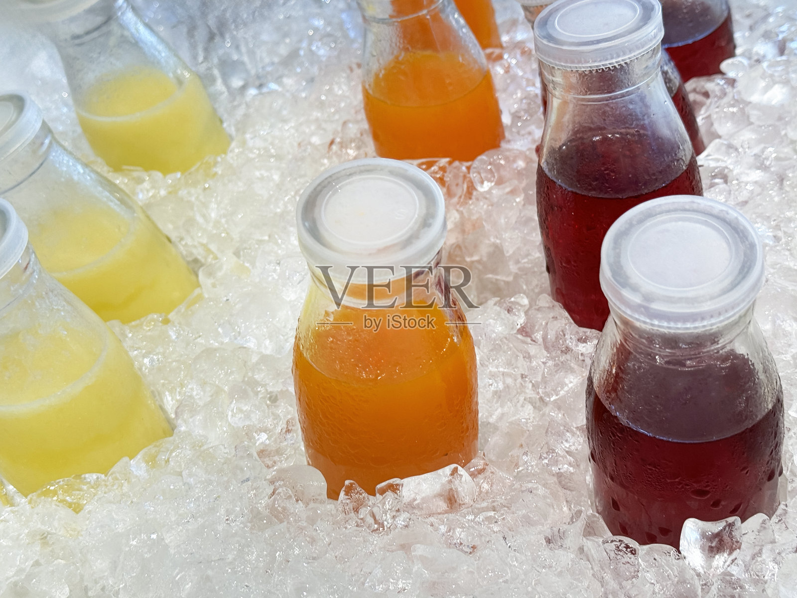 全画幅图片，金属托盘里装满了冰镇的冷果汁饮料，周围是冰块、碎冰和螺旋盖的菠萝汁、橙汁和蔓越莓汁，不含酒精的饮料装在玻璃瓶里，上面有冷凝物，高架视图照片摄影图片