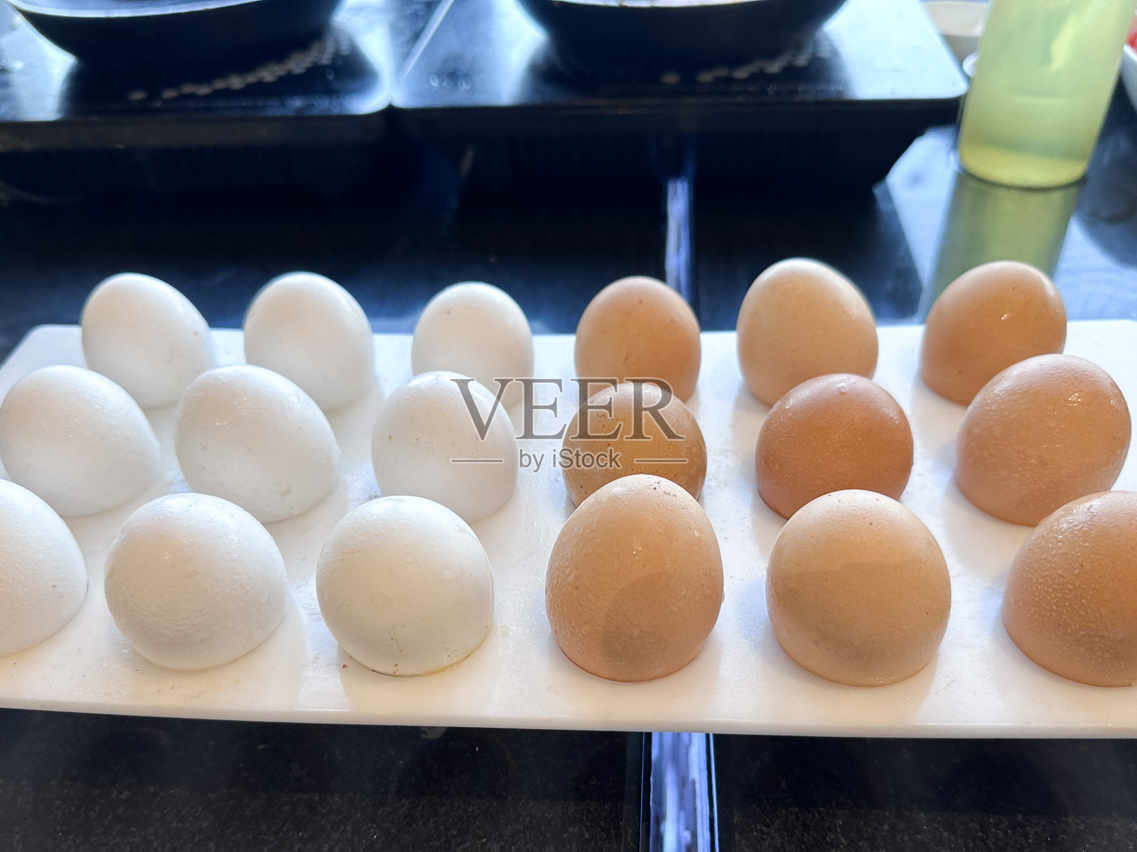 图片中的酒窝托盘上的白色和棕色的带壳鸡蛋，临时的，酒店自助早餐自助鸡蛋站的煎蛋卷，煎蛋和炒蛋，便携式电磁炉烹饪区背景，塑料瓶食用油，重点在前景照片摄影图片