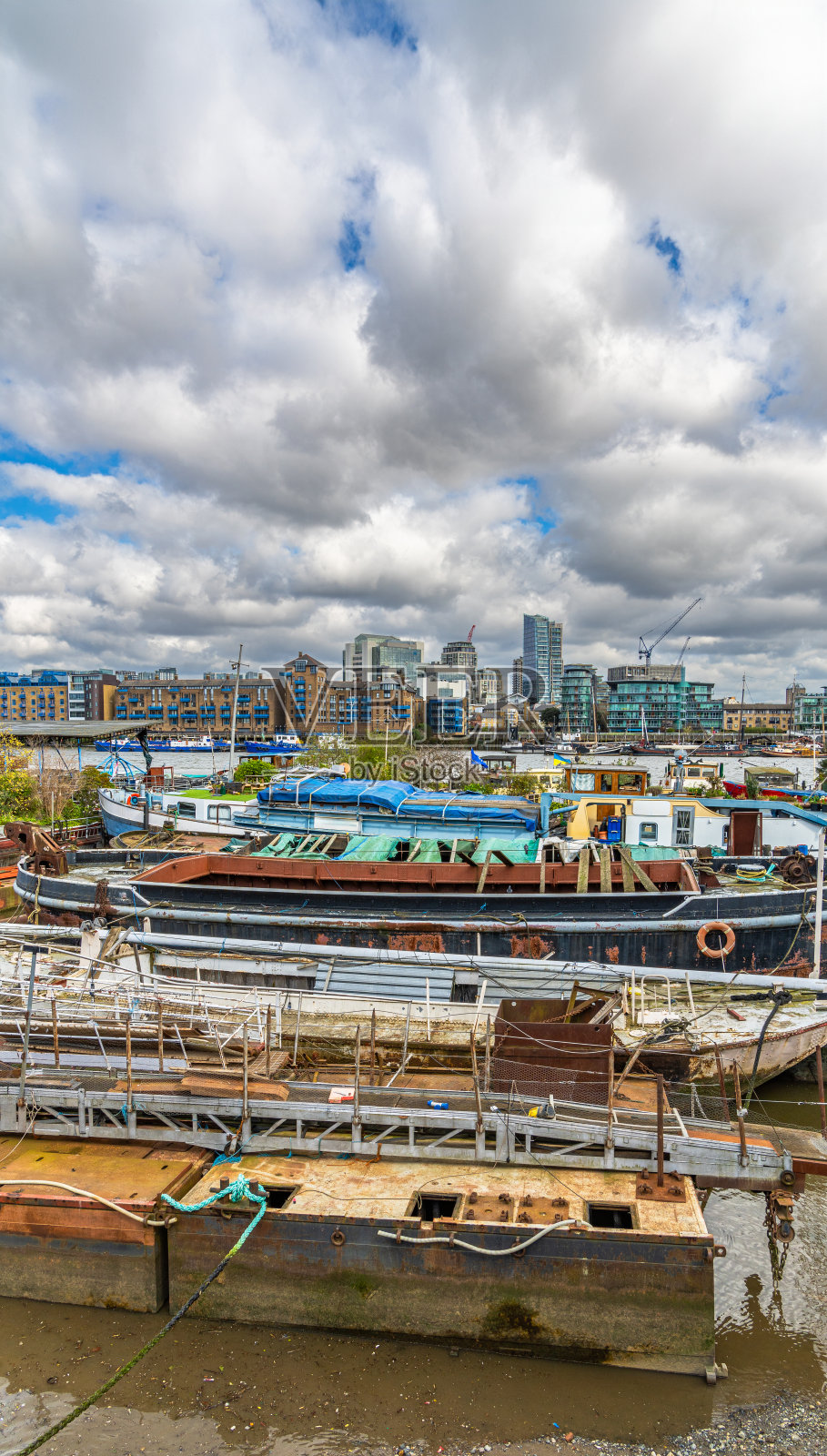 娱乐船和一些破旧的船停泊在英国伦敦巴特勒码头的泰晤士河岸边。照片摄影图片