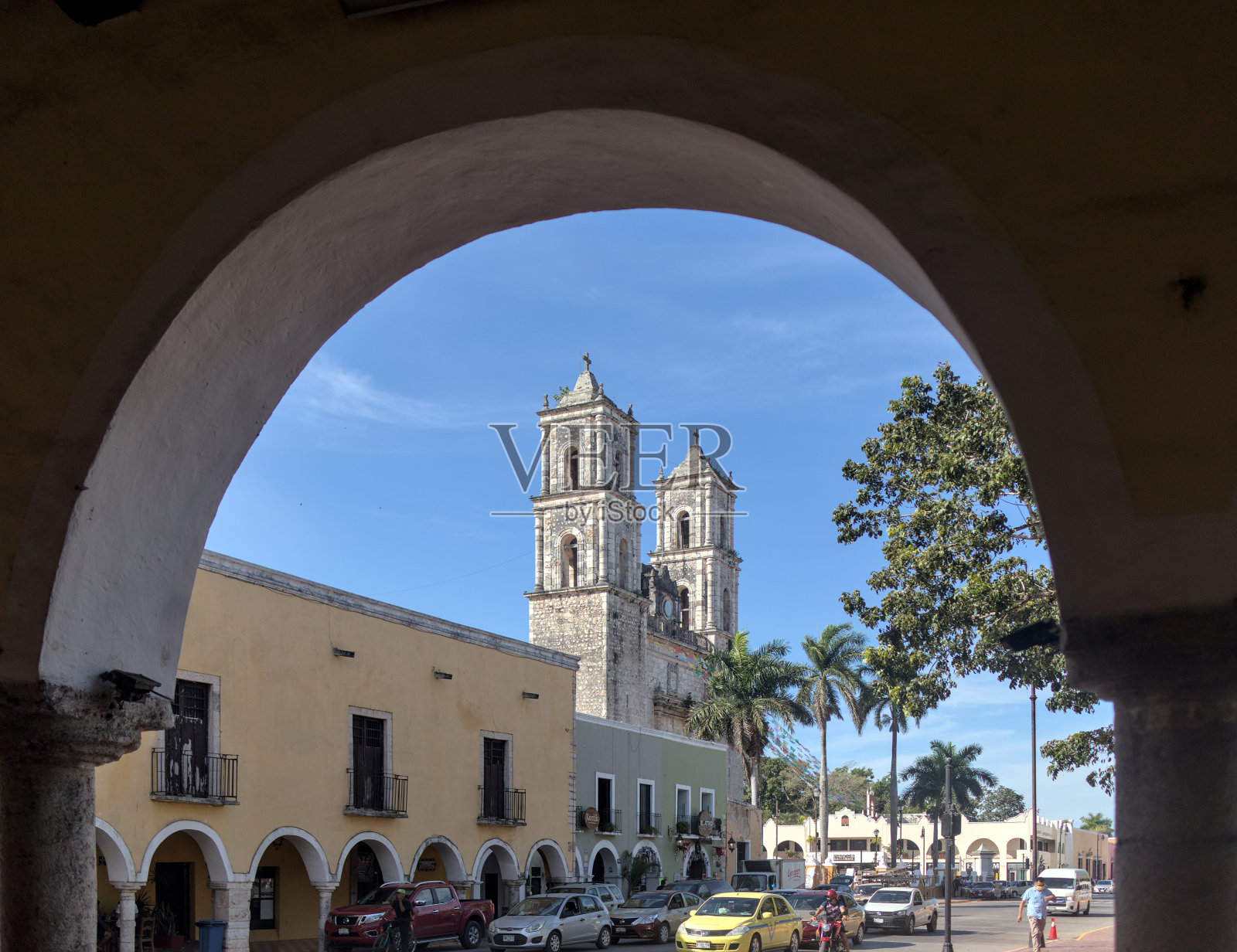 在墨西哥尤卡坦半岛的巴利亚多利德，透过拱门可以看到圣Servacio教堂前的41号路口，汽车停在路口等待绿灯。照片摄影图片