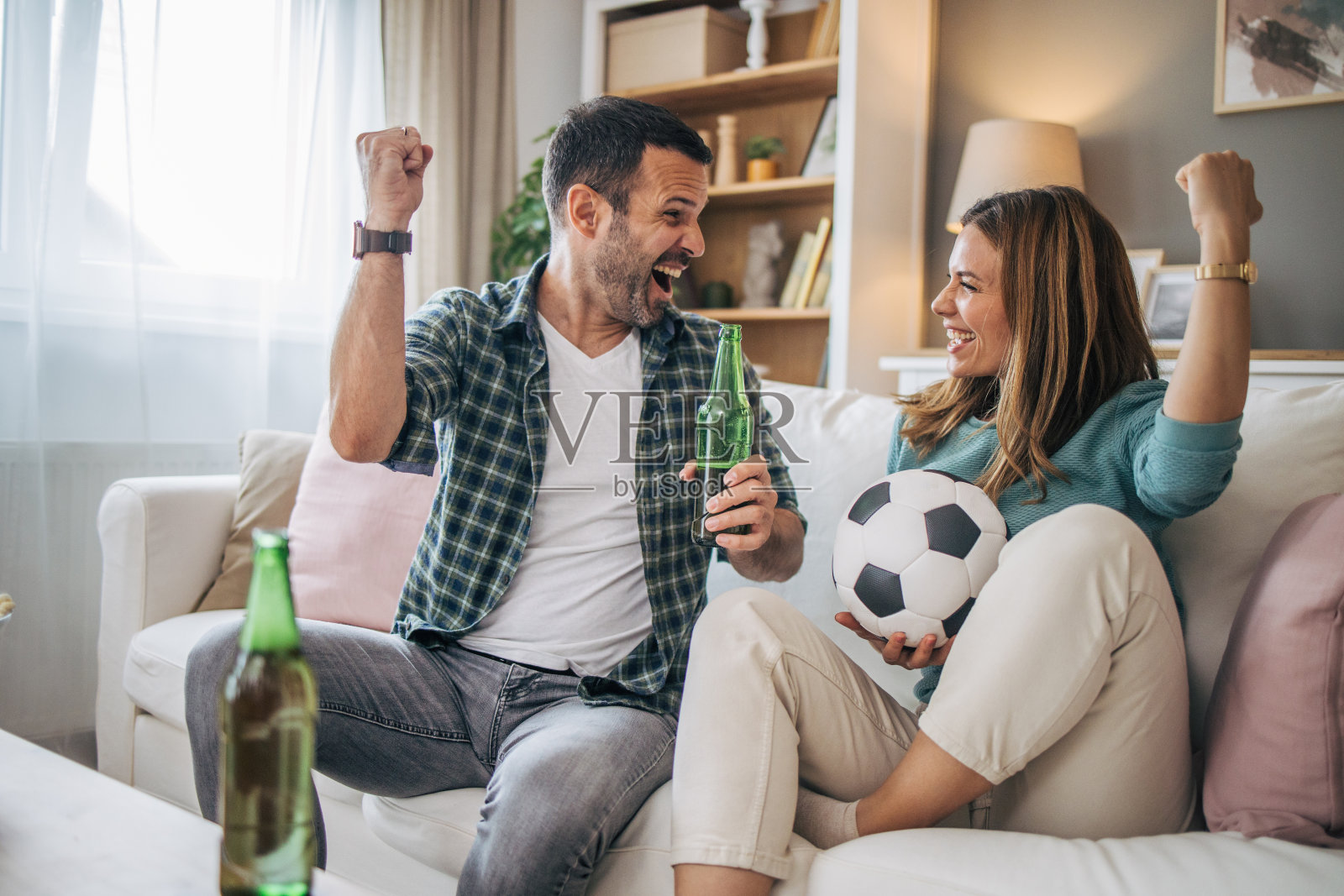幸福的情侣在家里一起度过周末，坐在沙发上看电视直播的足球比赛，为自己喜欢的球队加油照片摄影图片