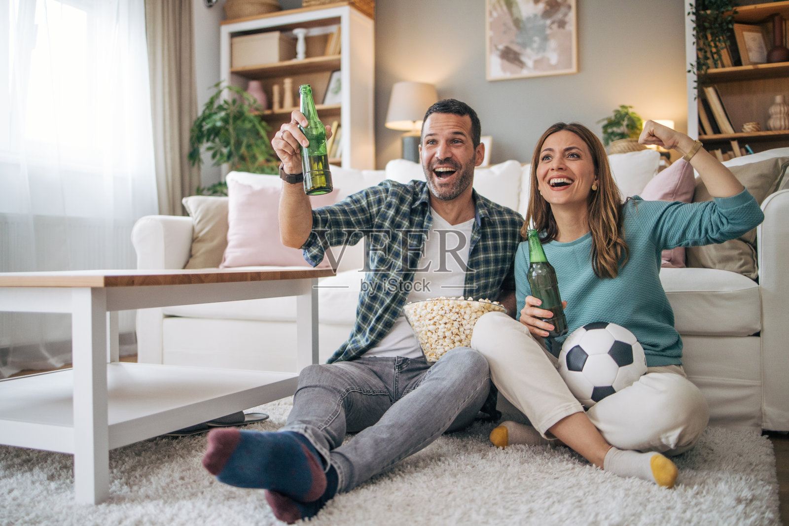 幸福的情侣在家里一起度过周末，坐在沙发上看电视直播的足球比赛，为自己喜欢的球队加油照片摄影图片