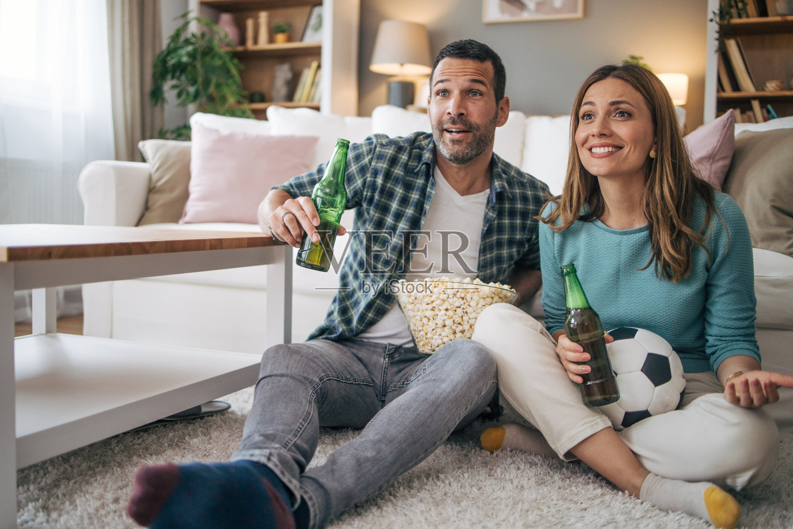 一对年轻夫妇在家里喝着啤酒，吃着爆米花，一边看电视上的足球比赛照片摄影图片